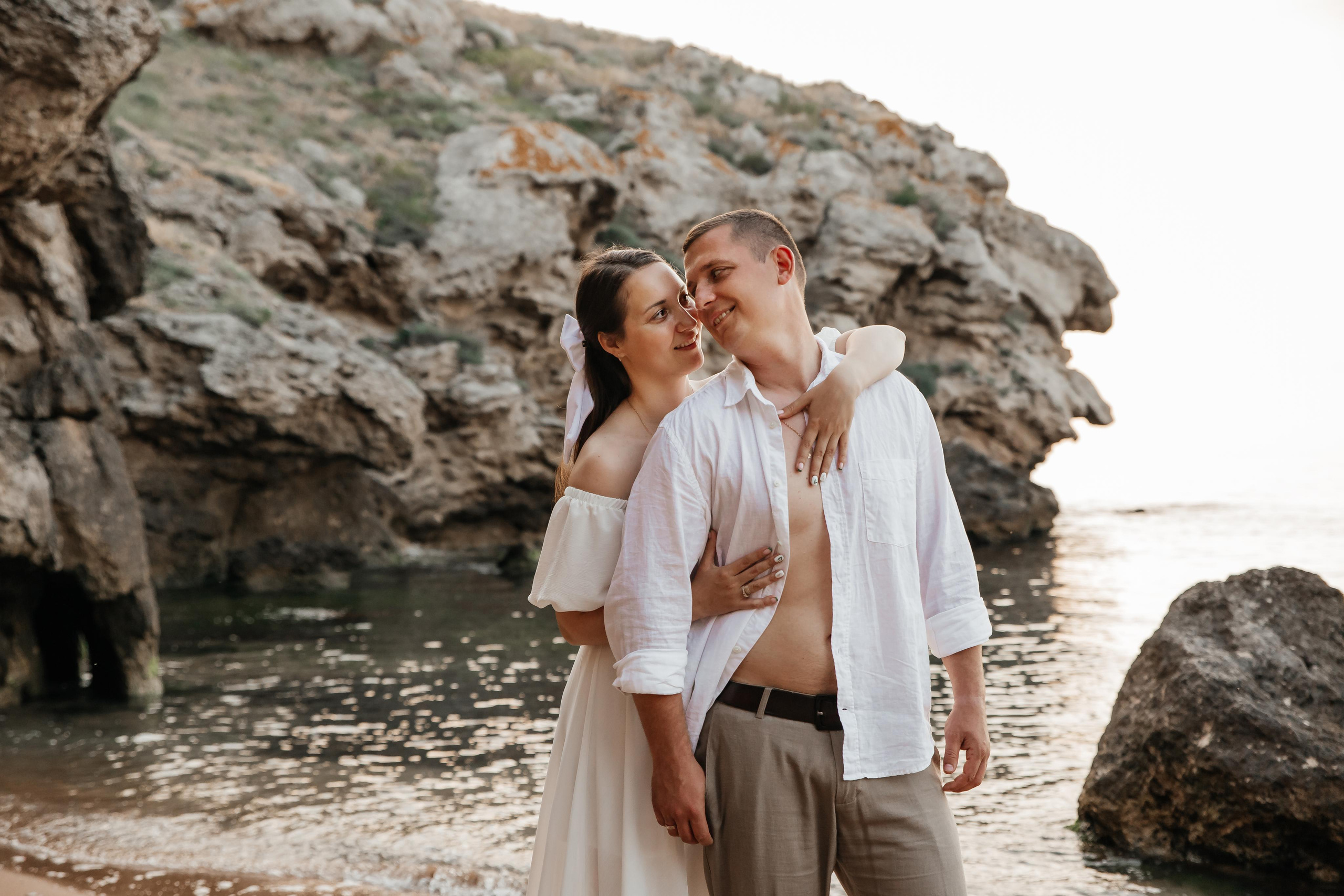 На переднем плане парень и девушка обнимающая его сзади на фоне скал. 