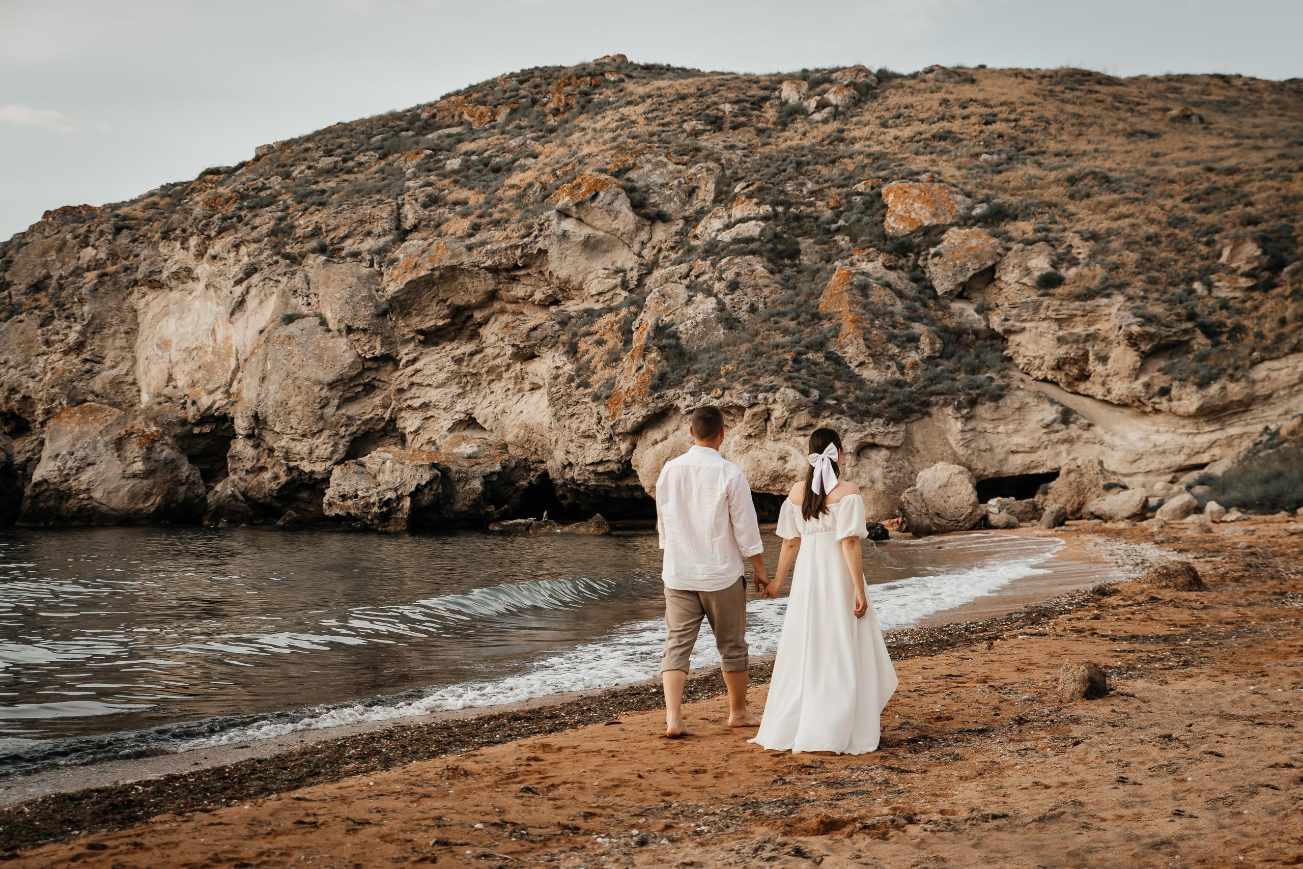 Красивая пара гуляет по берегу моря на фоне скал.