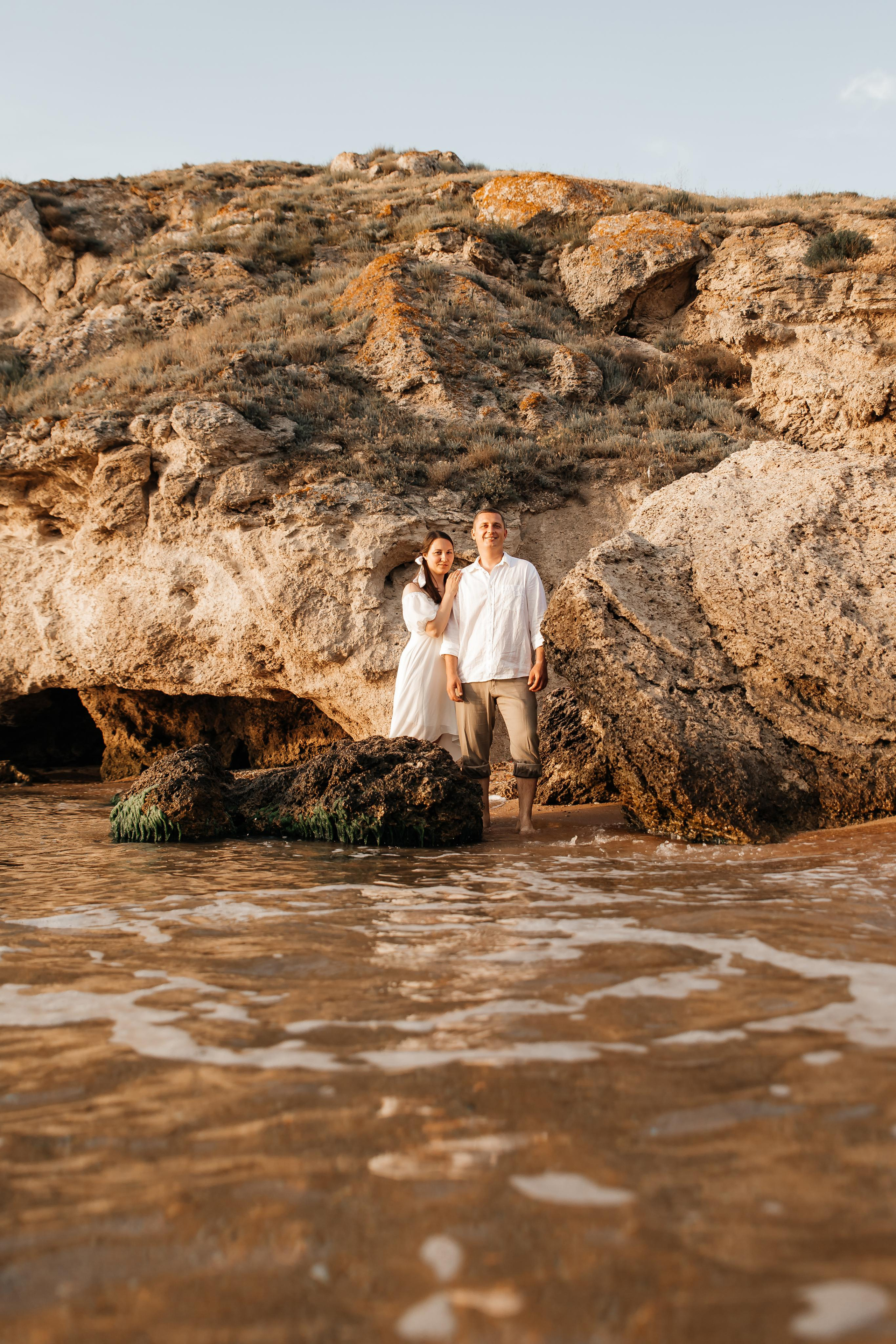 Девушка и парень стоят среди больших камней на фоне гор на морском побережье. 