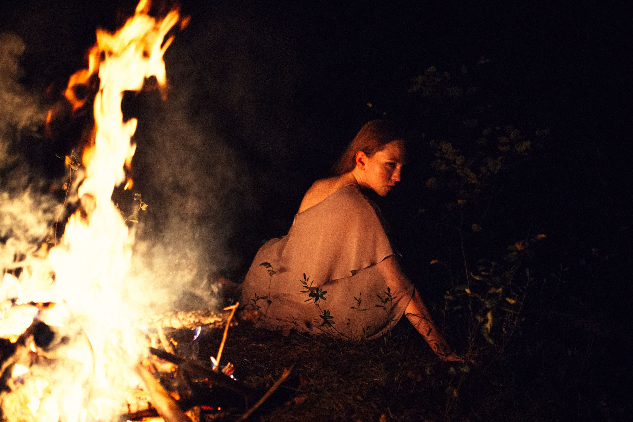 Рыжеволосая девушка сидит рядом с костром