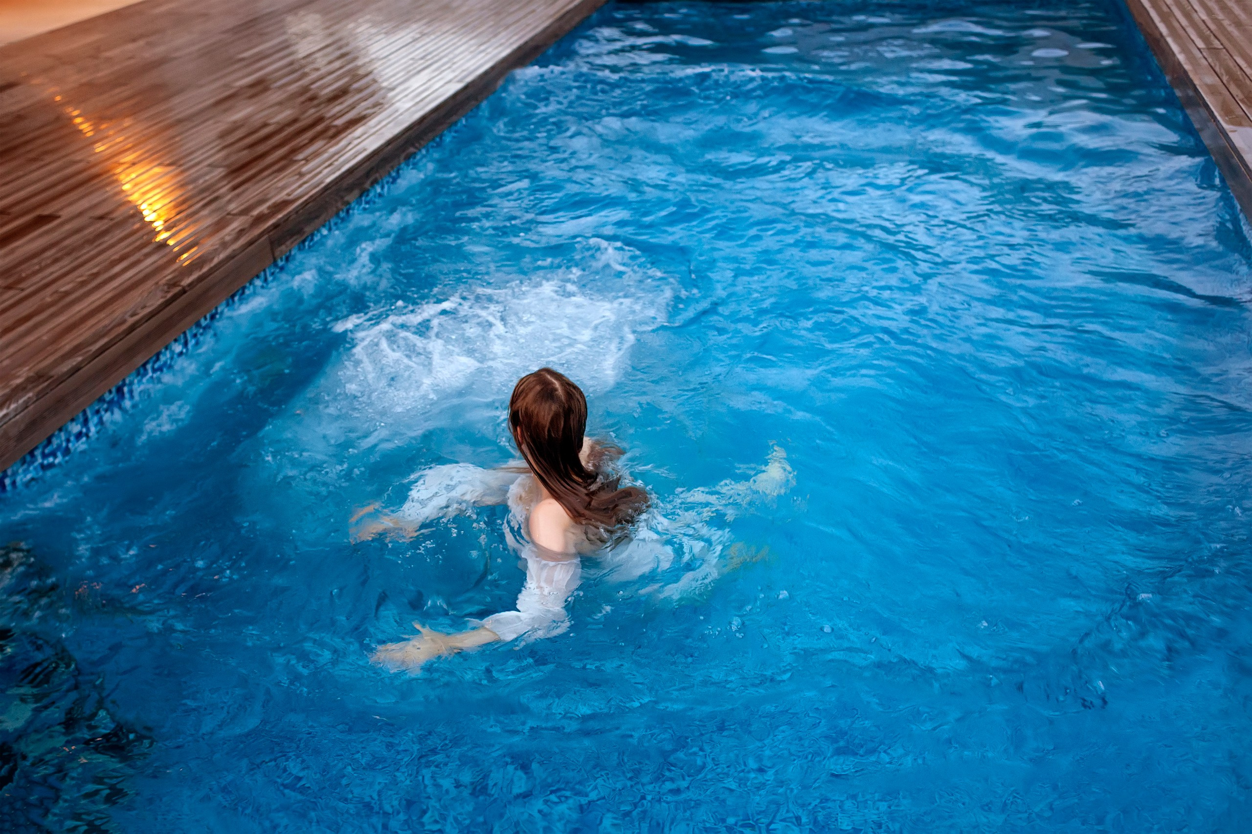 Девушка плавает в бассейне с голубой водой