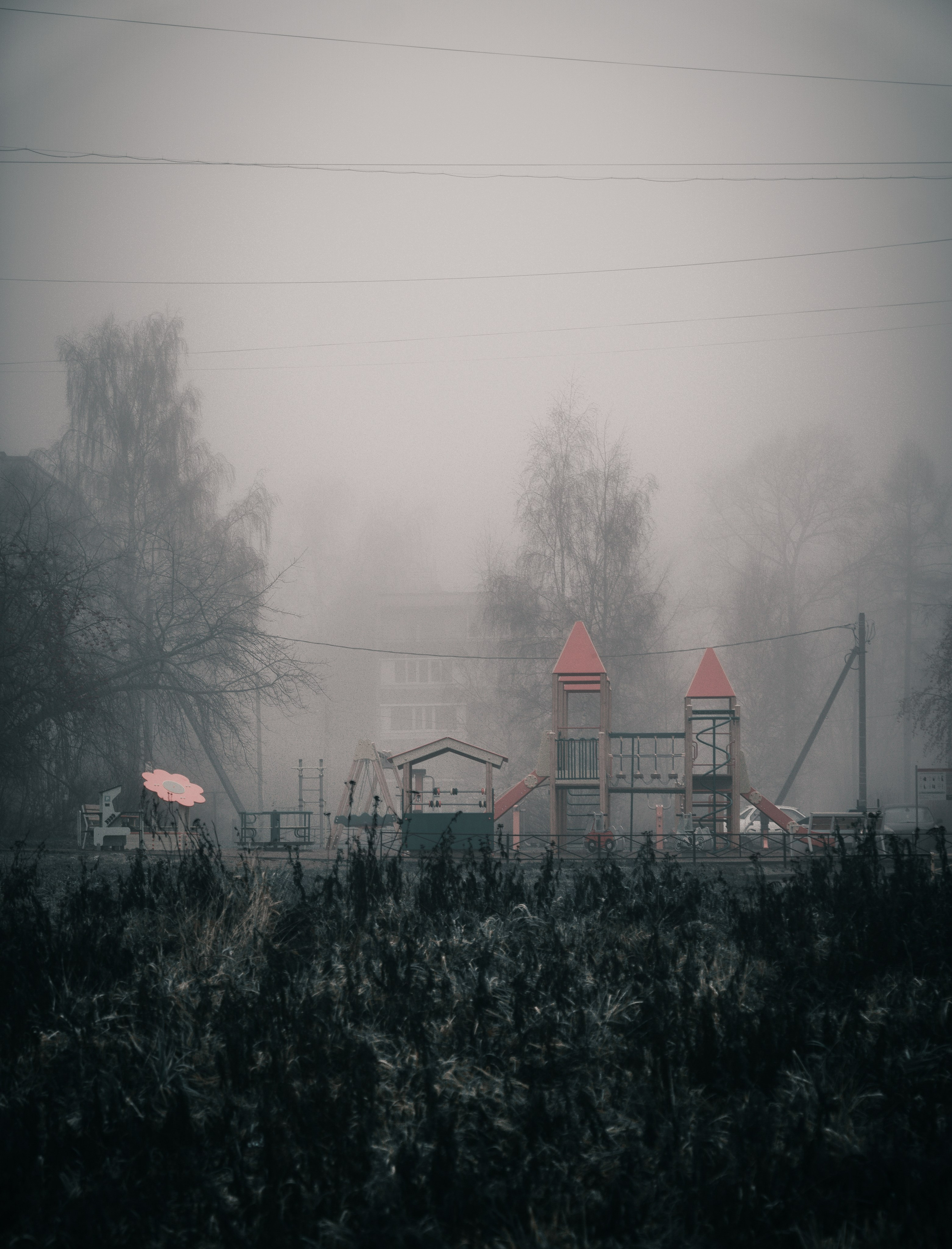 Детская площадка в тумане среди панельных домов Санкт-Петербурга, яркие игровые элементы в сером мареве, уличная фотография спального района Питера, Evrednix — Евгений Мальцев.