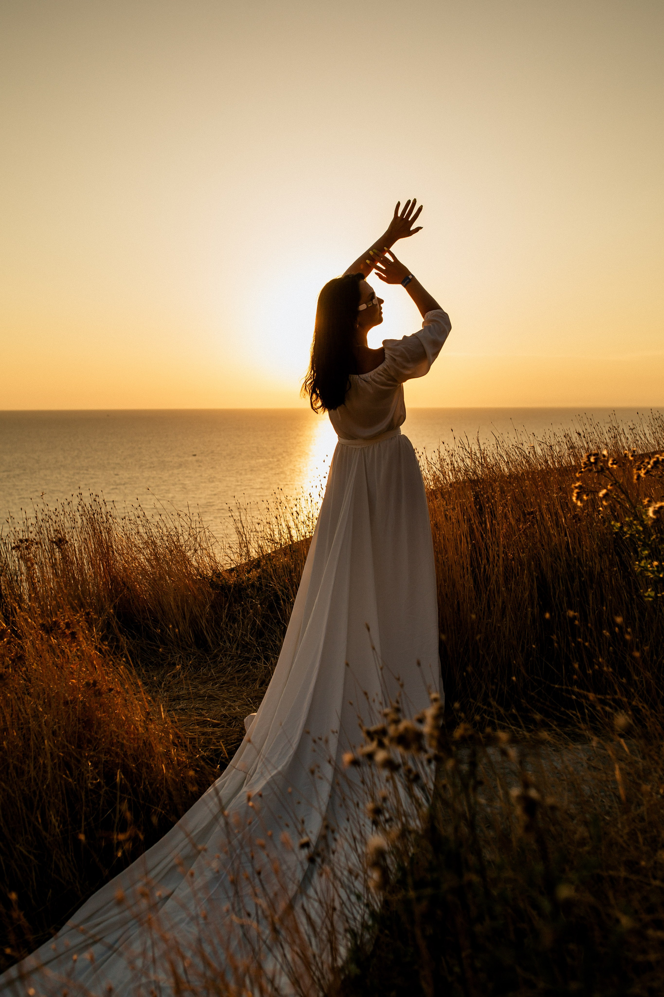 Силуэт невесты в красивом белом платье на фоне закатного солнца.