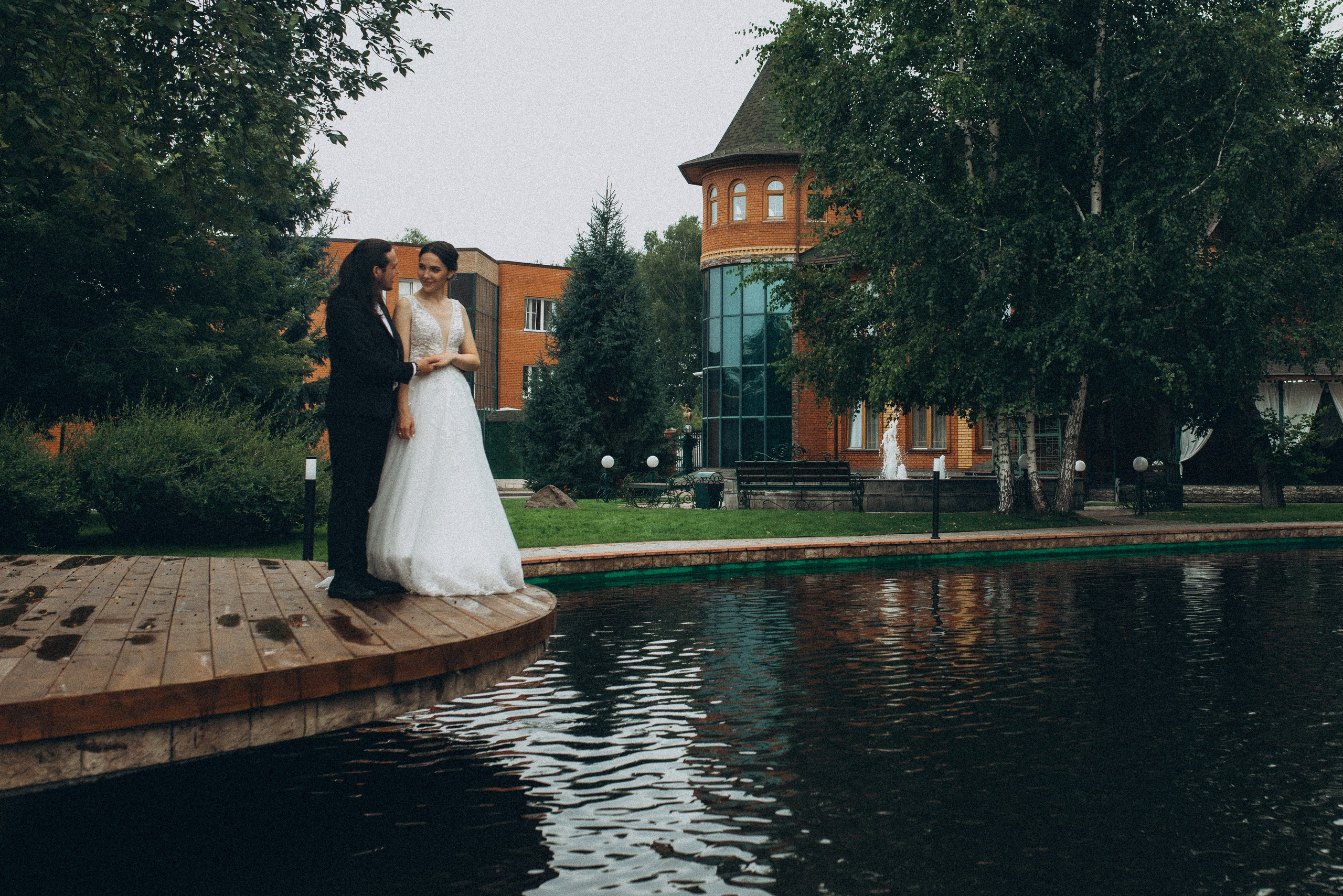 Невеста Линда и жених Никита держатся за руки на деревянном пирсе у пруда. Свадебная фотосессия на природе.