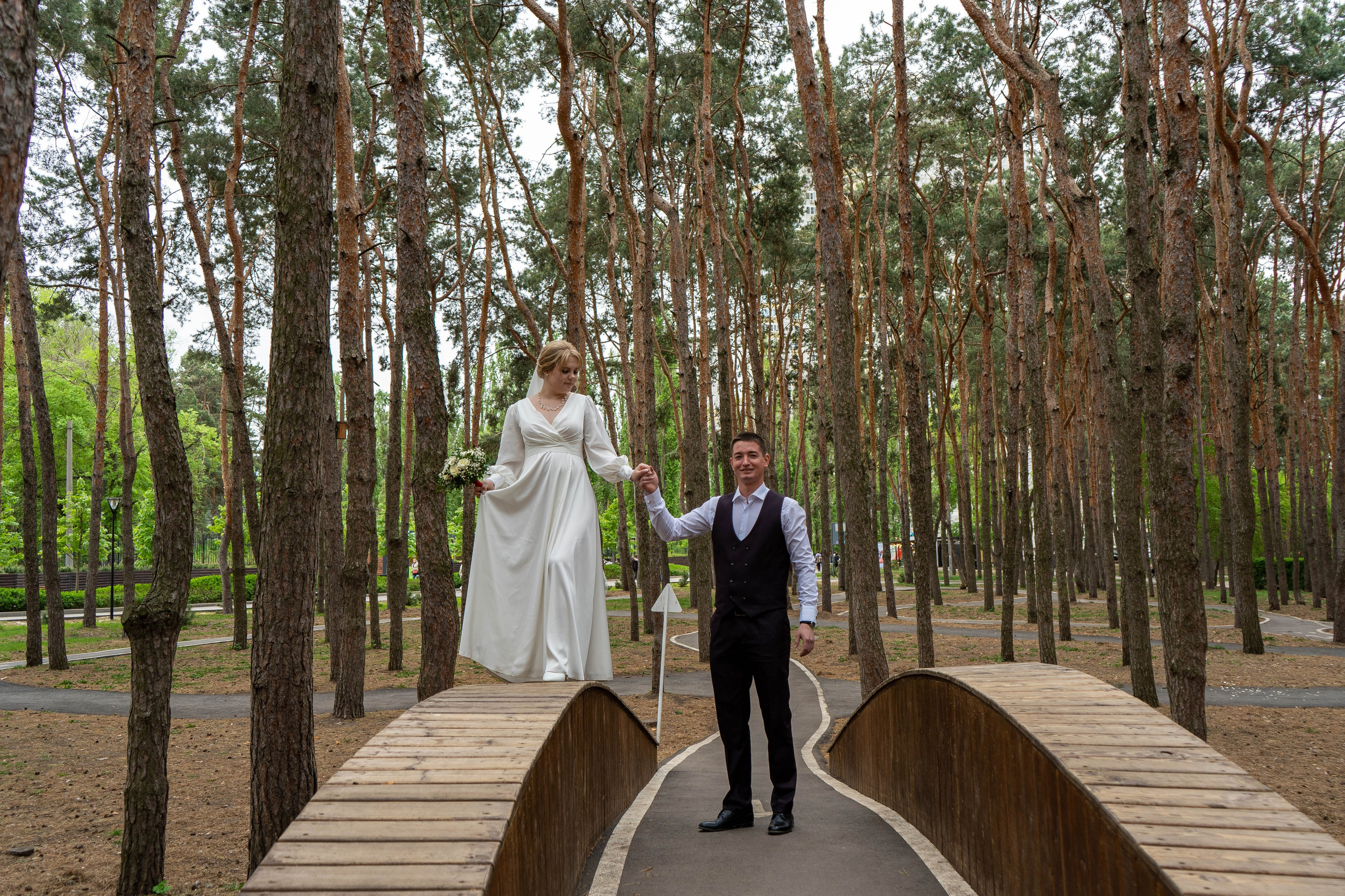 Жених держит невесту за руку на мосту в парке в Воронеже