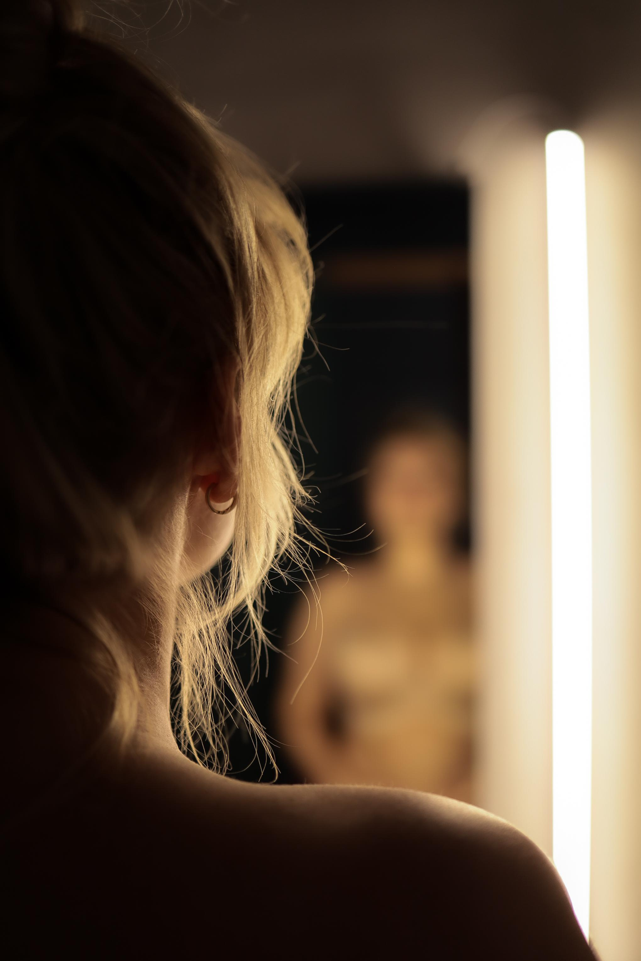 модель стоит у зеркала  примерочной в контровом свете 