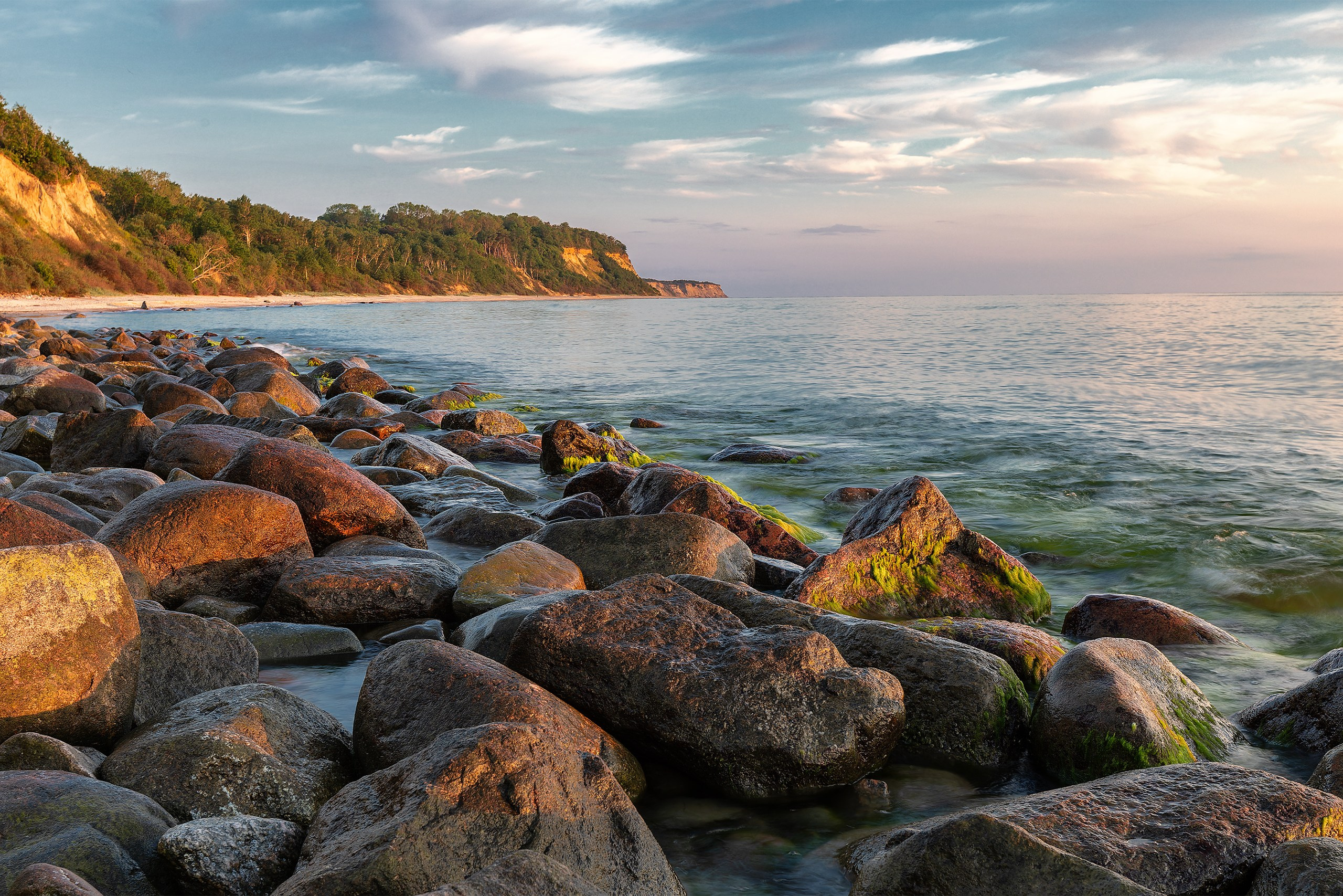 A rocky beach with large boulders at Brüsterort coast in East Prussia during a summer sunset.