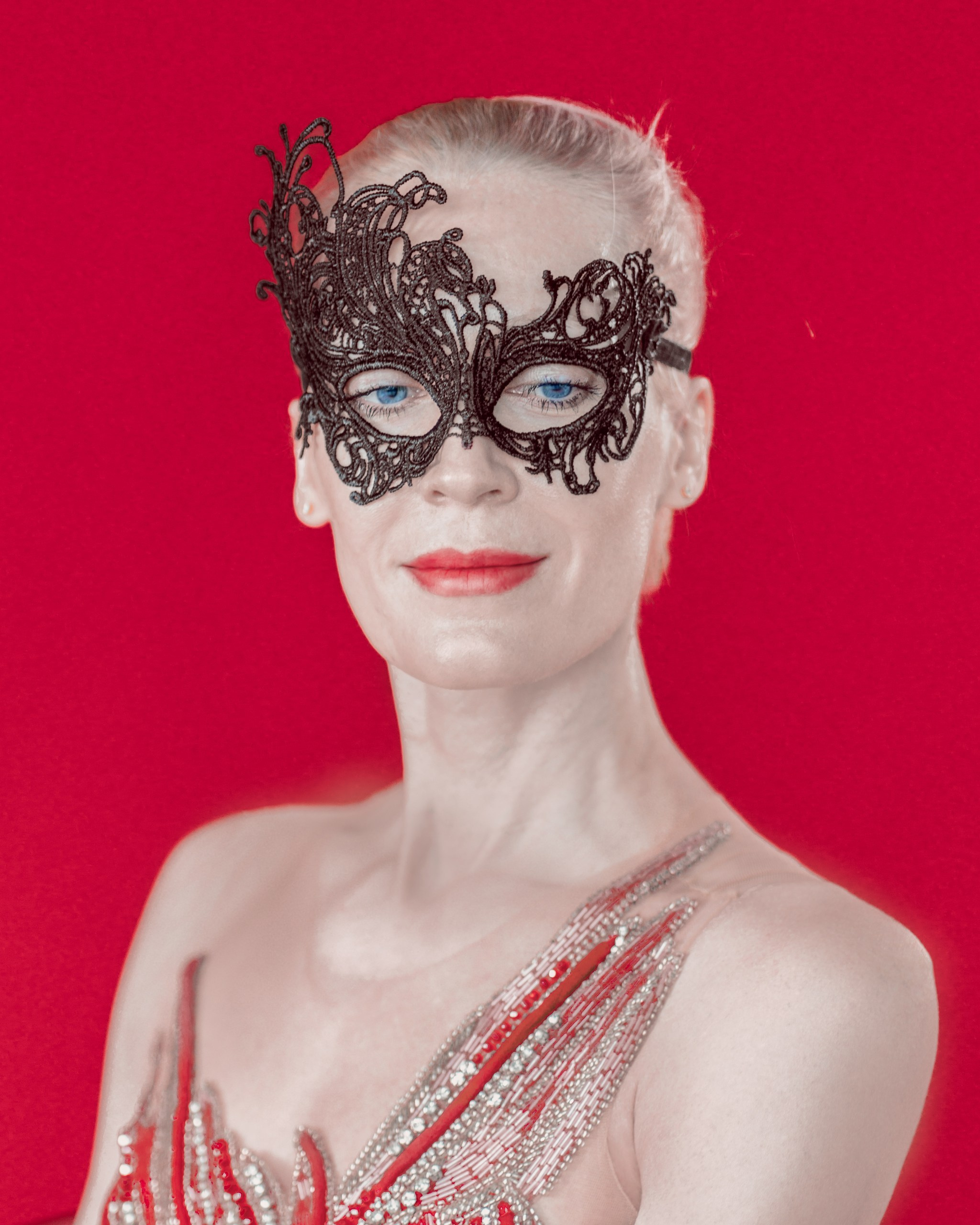 Mysterious female photo shoot in Yekaterinburg studio. Portrait in a mask in close-up, on a red background.