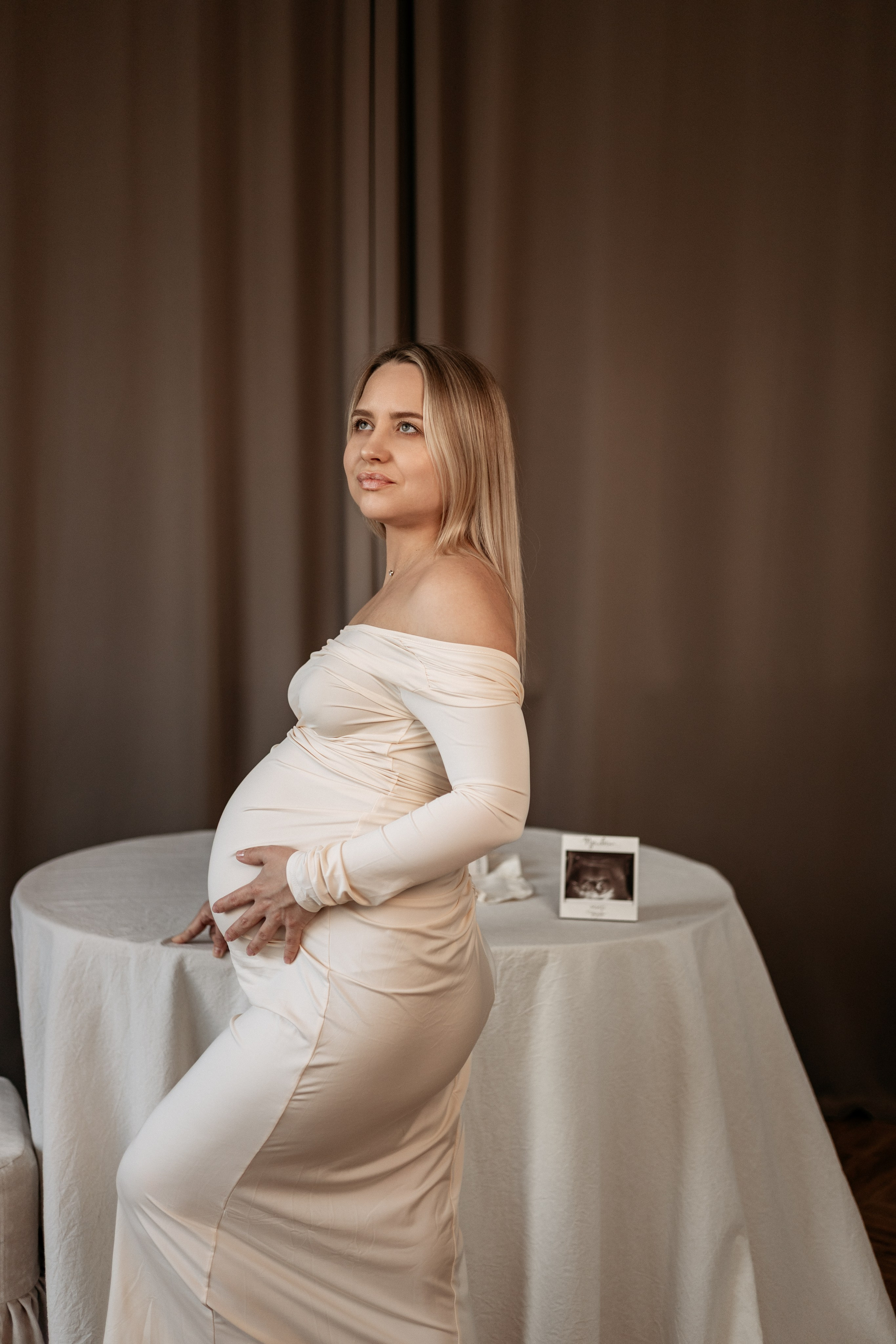 Осенняя фотосессия беременности: будущая мама в вязаном свитере и сапогах стоит в парке, золотые листья кружатся вокруг ее живота.