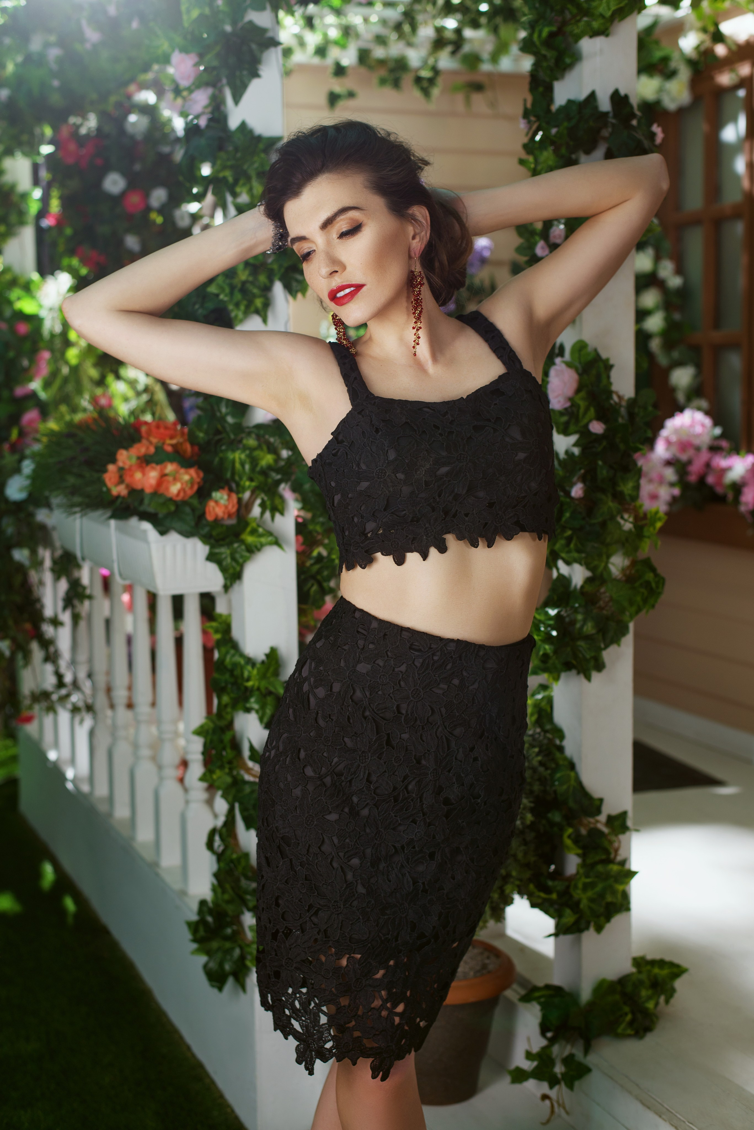 Девушка в костюме с коротким топом с закрытыми глазами на фоне солнечной веранды