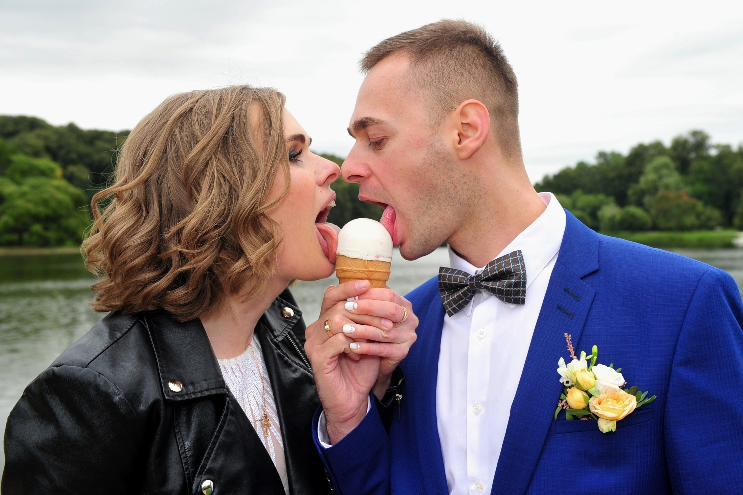 Свадьба в Царицыно хмурым прохладным летним днём, молодожены едят мороженое в вафельном стаканчике, новобрачные лижут языками шарик мороженого