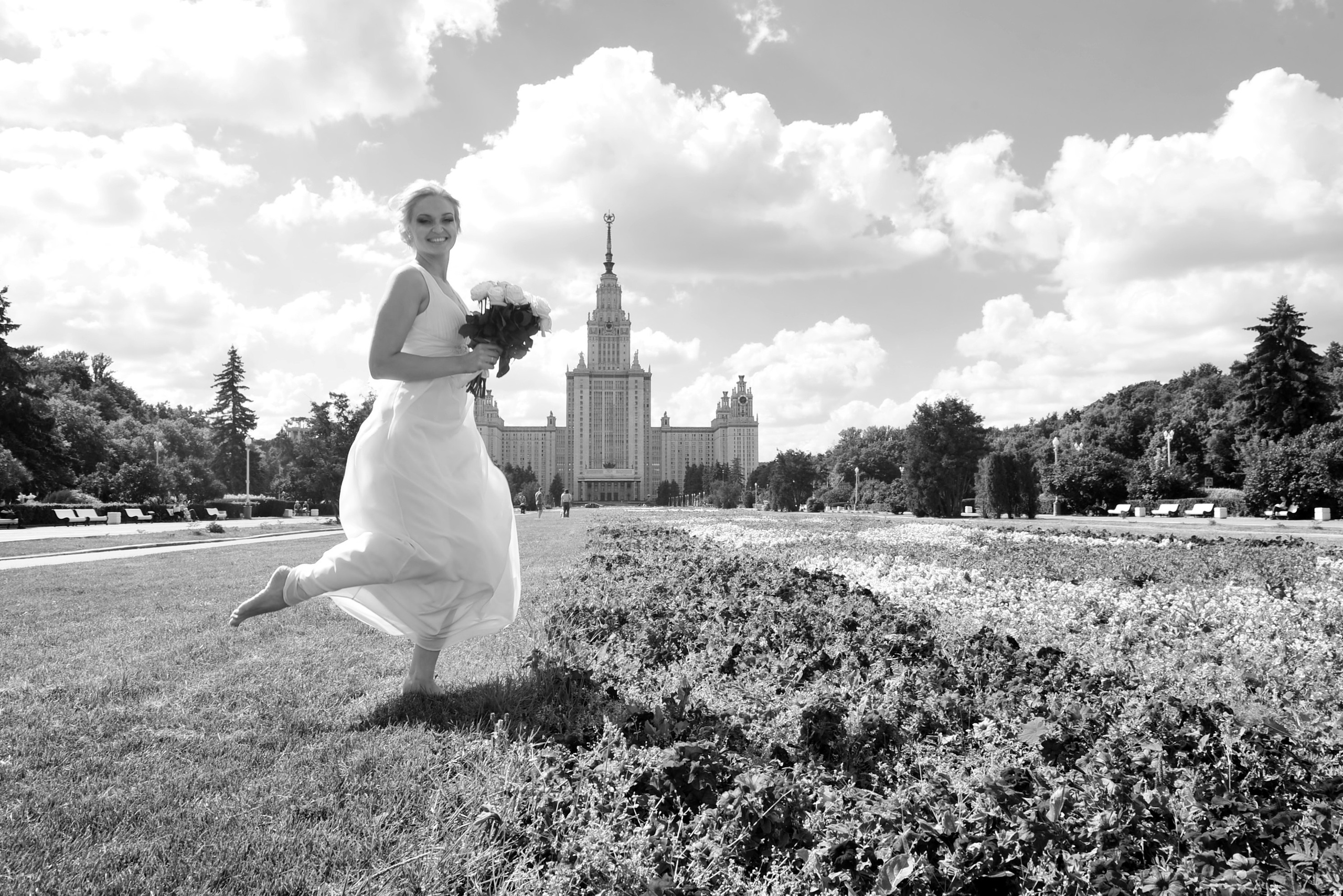 Свадьба на Воробьёвых Горах рядом с МГУ, невеста в полный рост позирует со свадебным букетом на фоне МГУ, черно-белая фотография