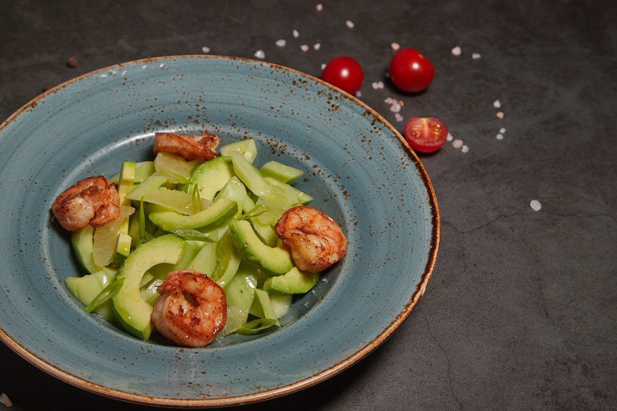 Фуд-фотография салата с авокадо и зеленью в голубой тарелке.