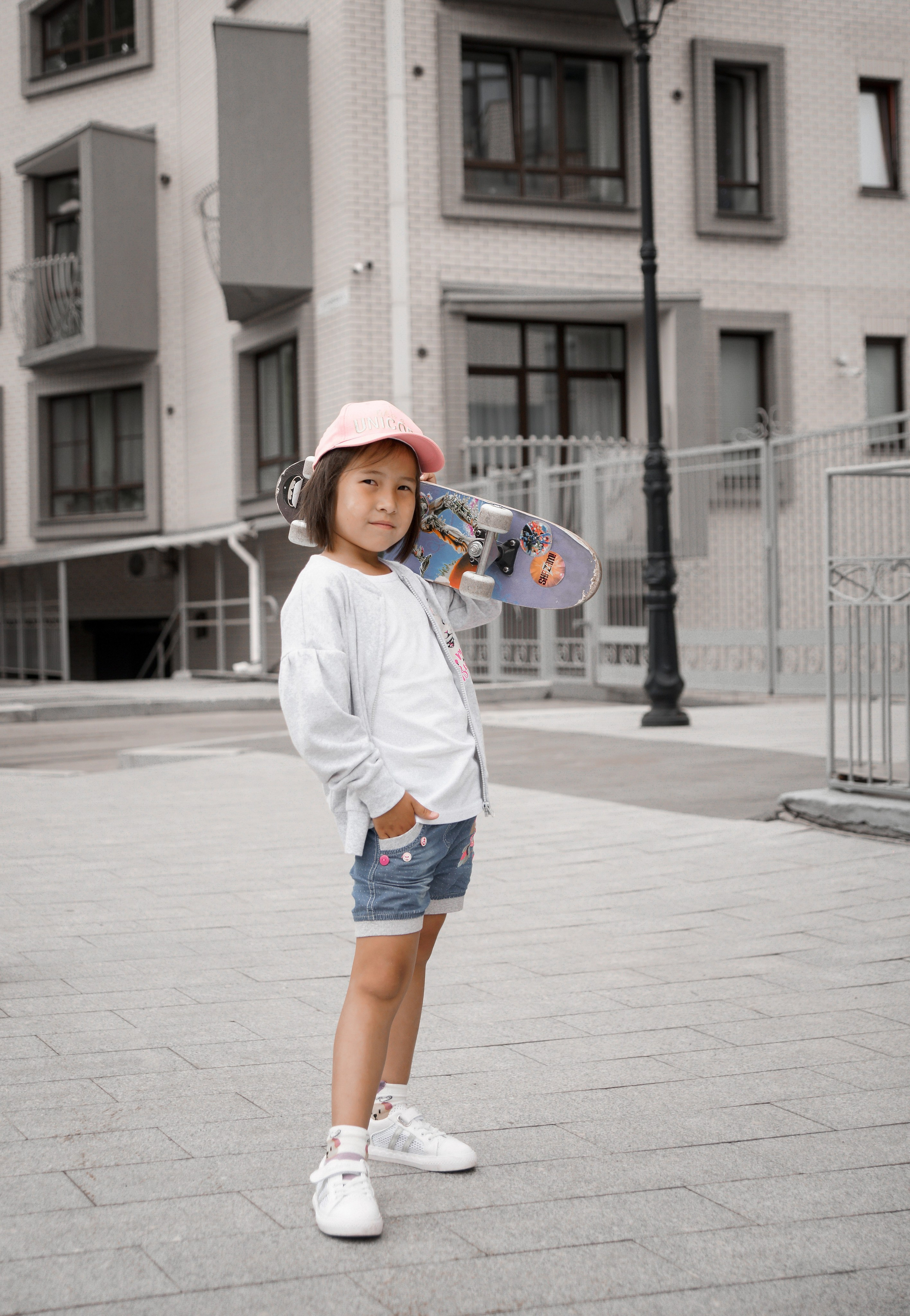 Детская фотосессия летом - девочка стоя в бейсболке со скейтом