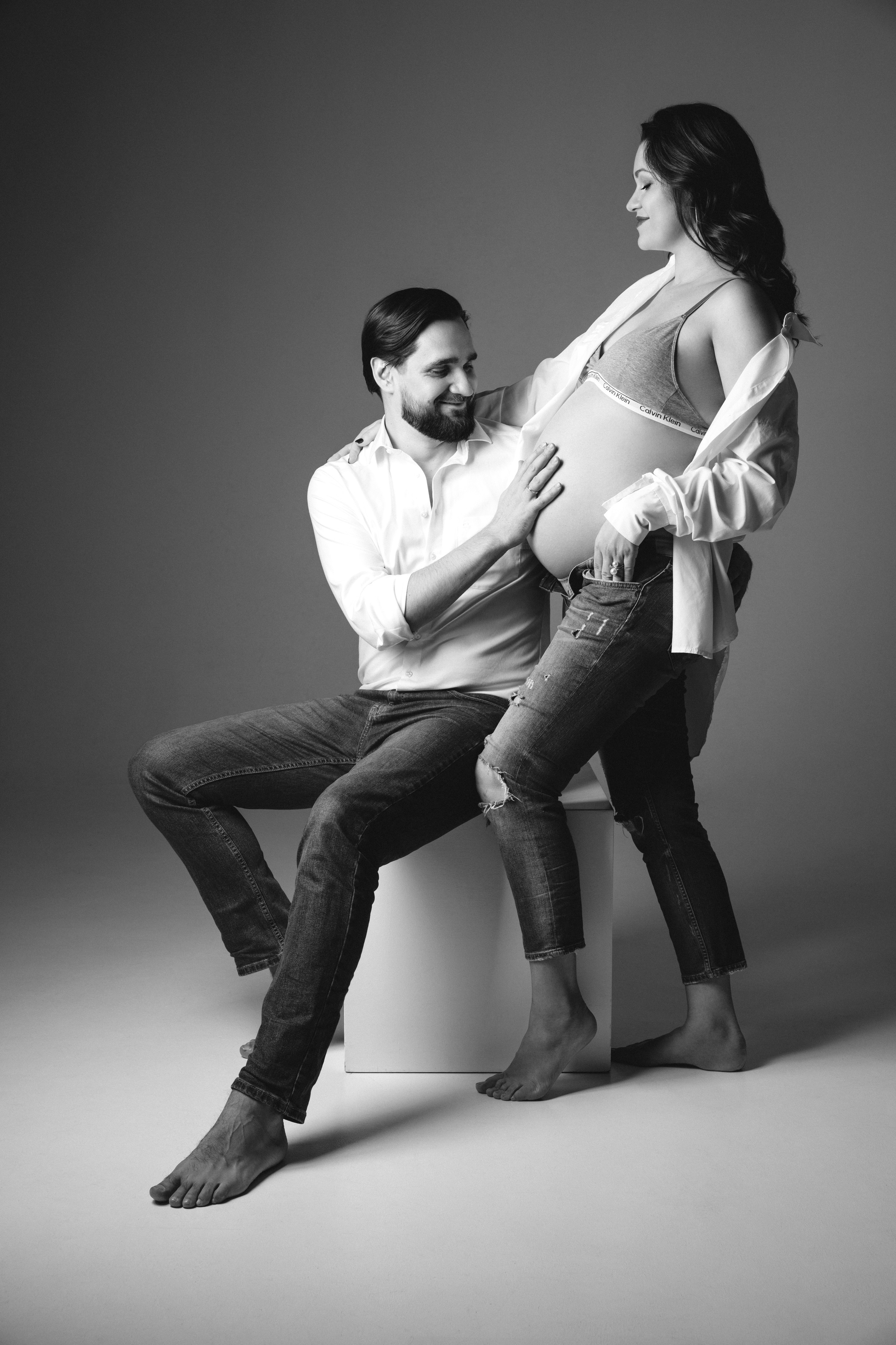 Черно-белая студийная фотосессия беременности в Москве с мужем на сером фоне.