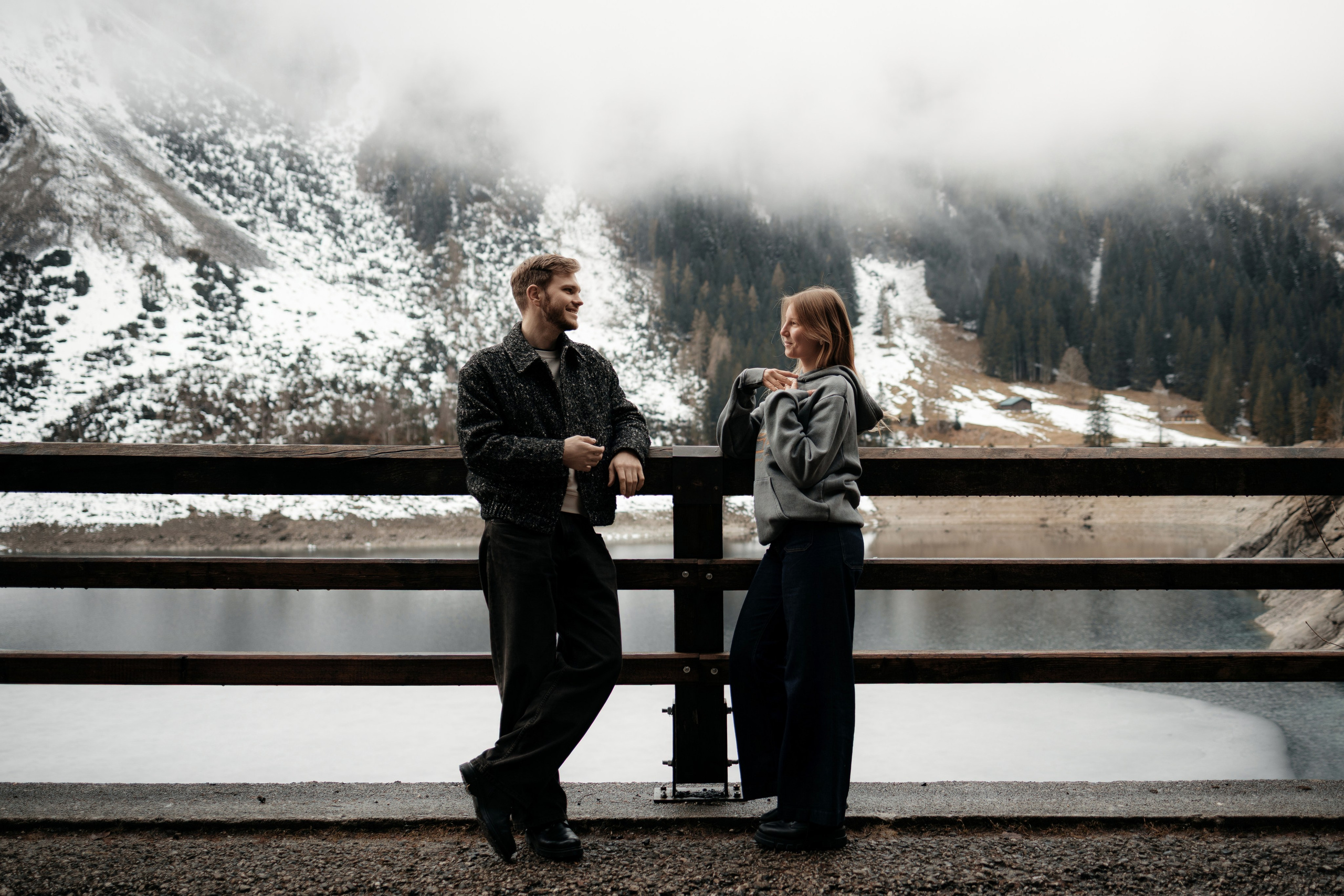 Пара стоит у моста с видом на горы, спокойная уличная сцена