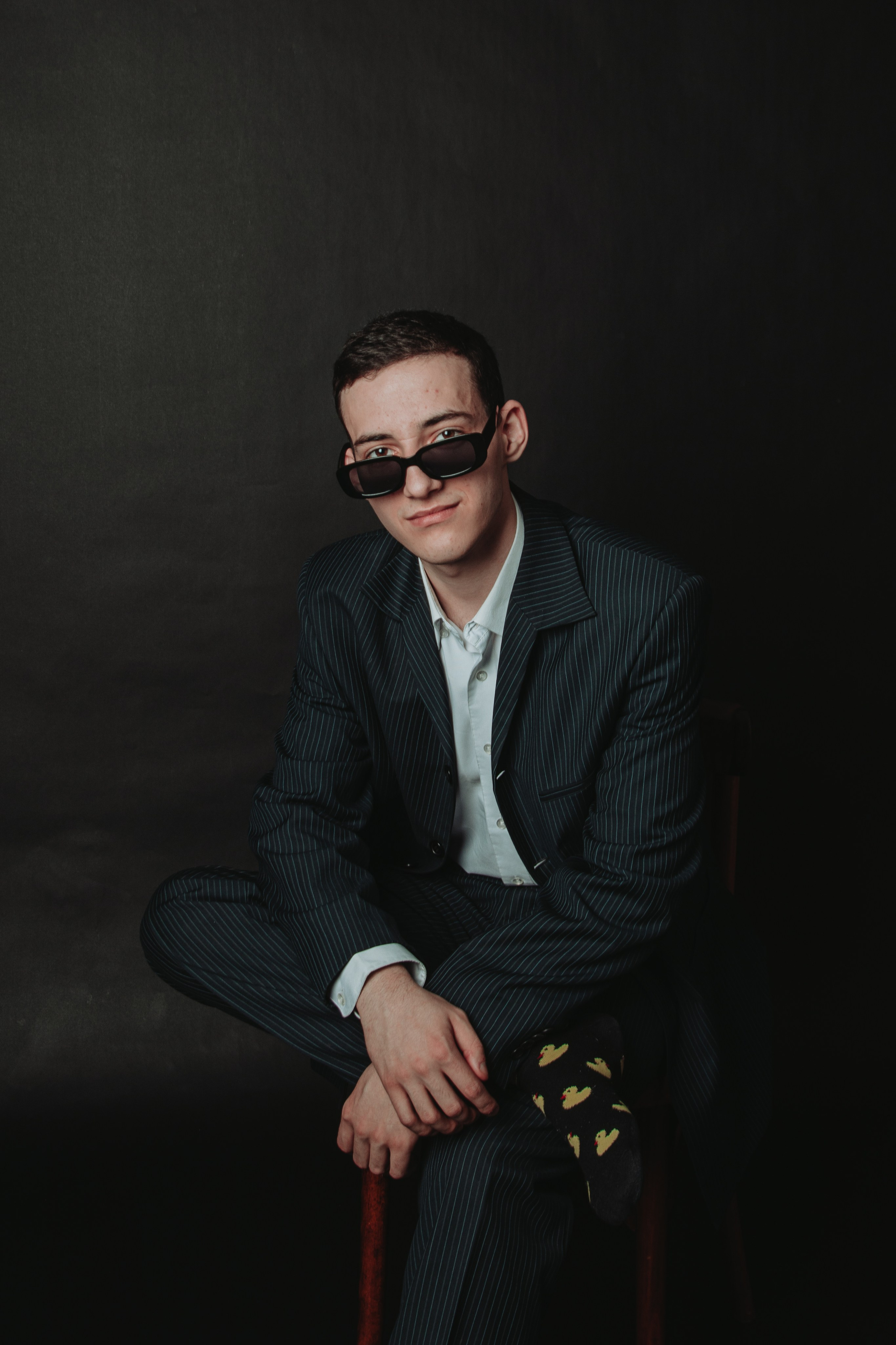парень на черном фоне в классическом костюме в черных очках и веселых носках фотосессия