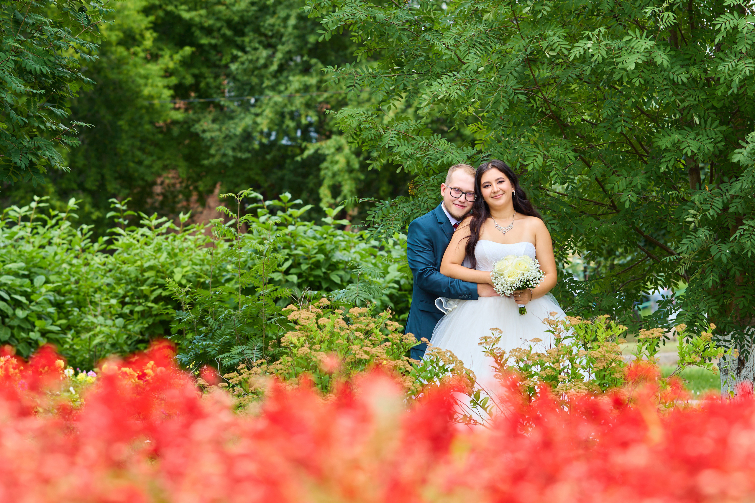 Жених сзади обнимает невесту, на переднем плане цветы