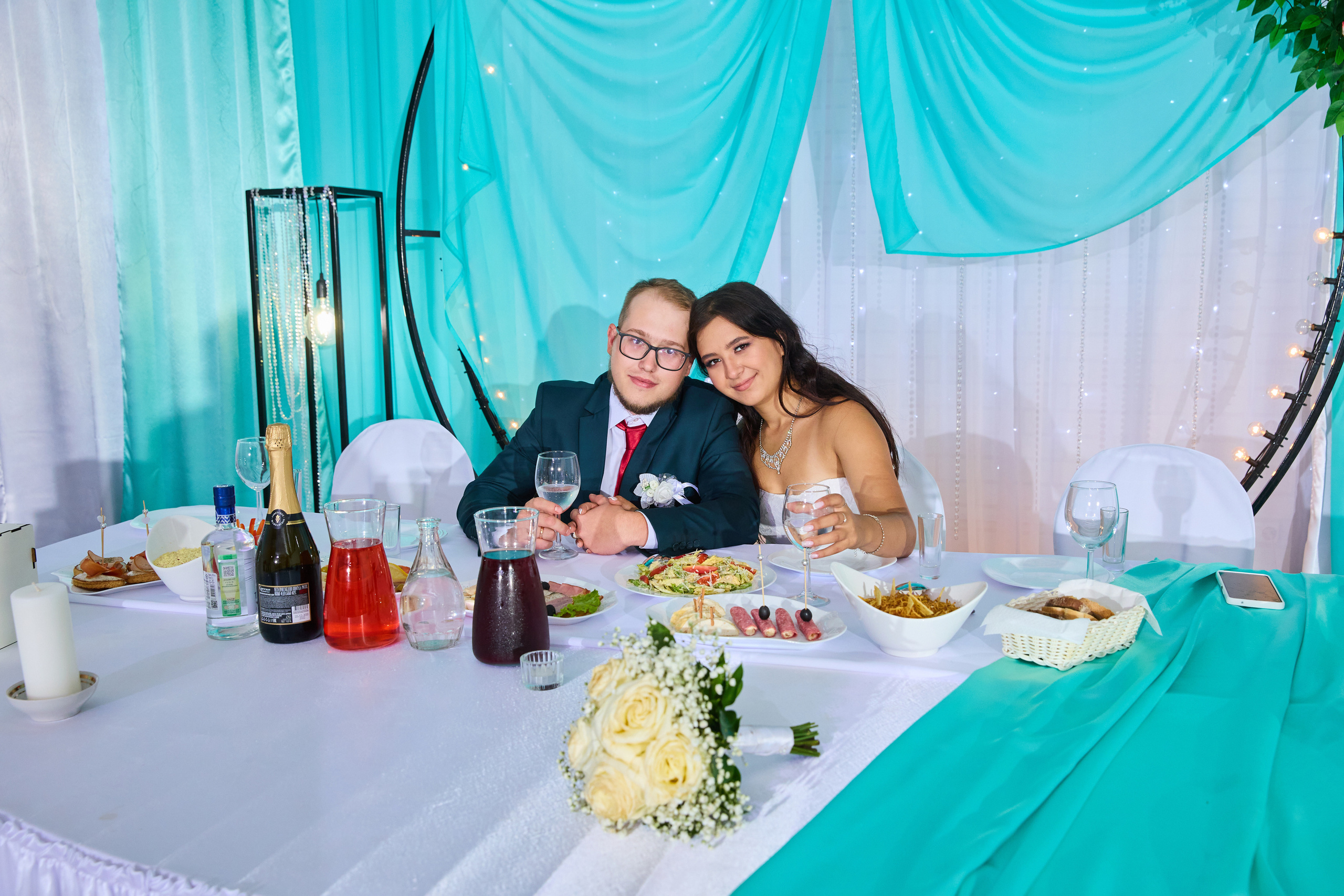 Жених и невеста на свадебном банкете сидят за украшенным столом