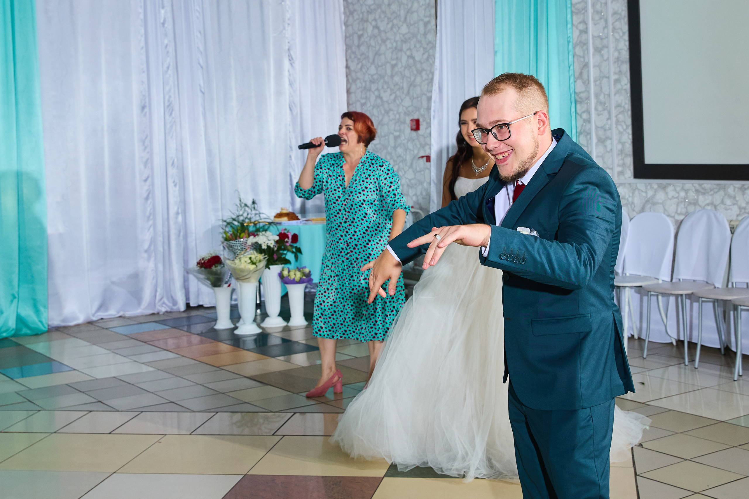 Жених обнимает невесту на заднем плане тамада