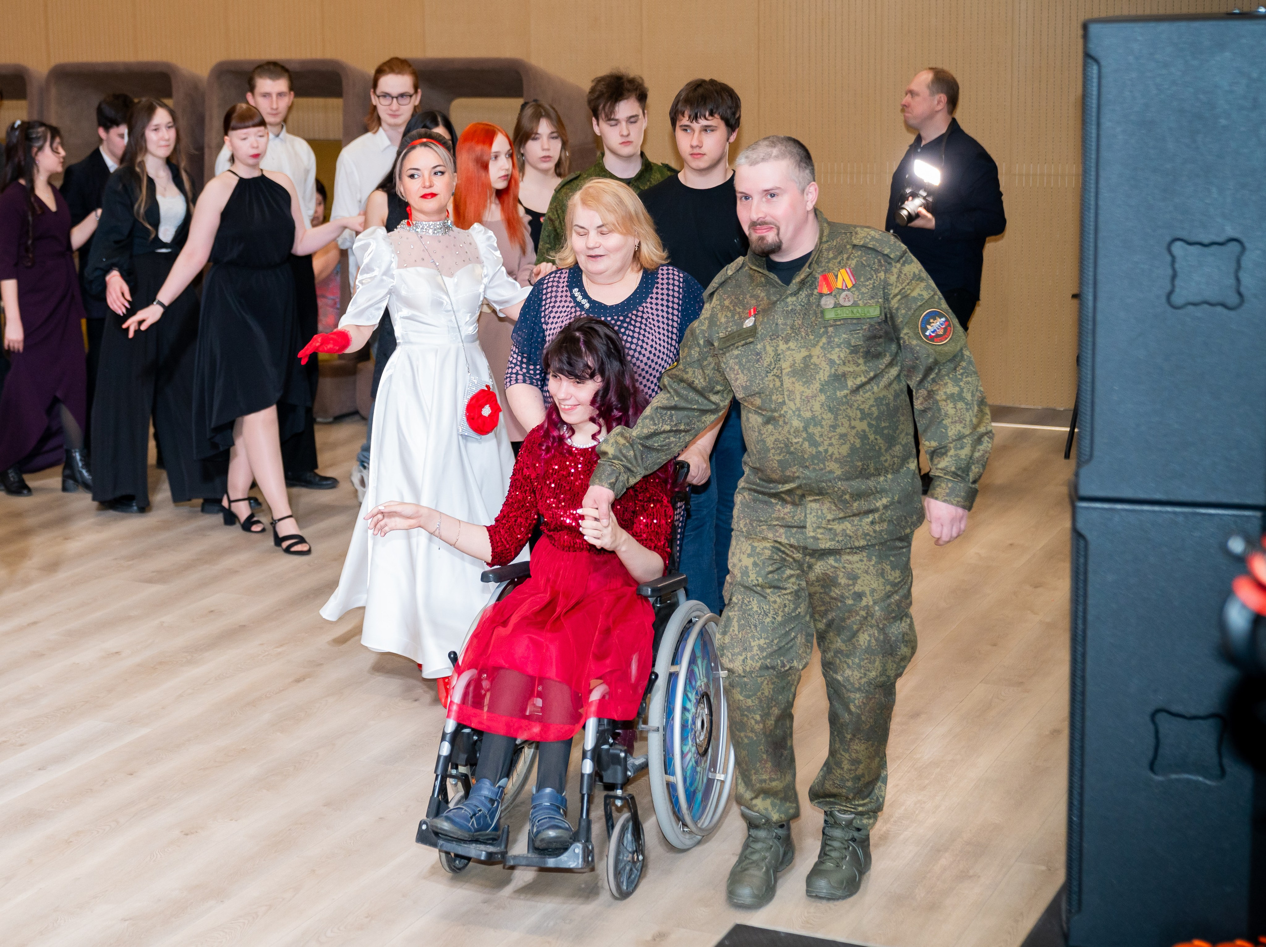 Мужчина в военной форме ведёт под руку девушку в красном платье на инвалидной коляске на инклюзивном балу «Мы все равны». Фотограф Мальцев Евгений.