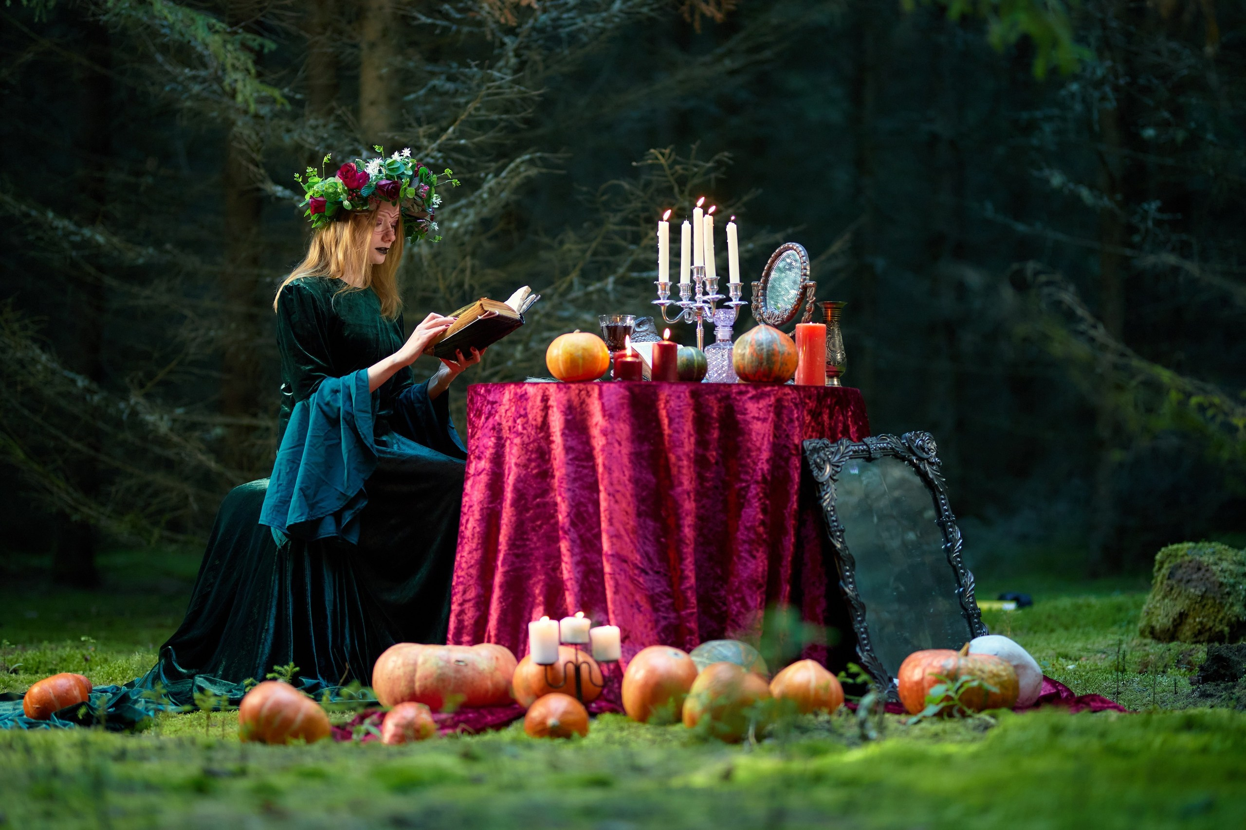 Колдунья читает заклинание из колдовской книги сидя за столом со свечами