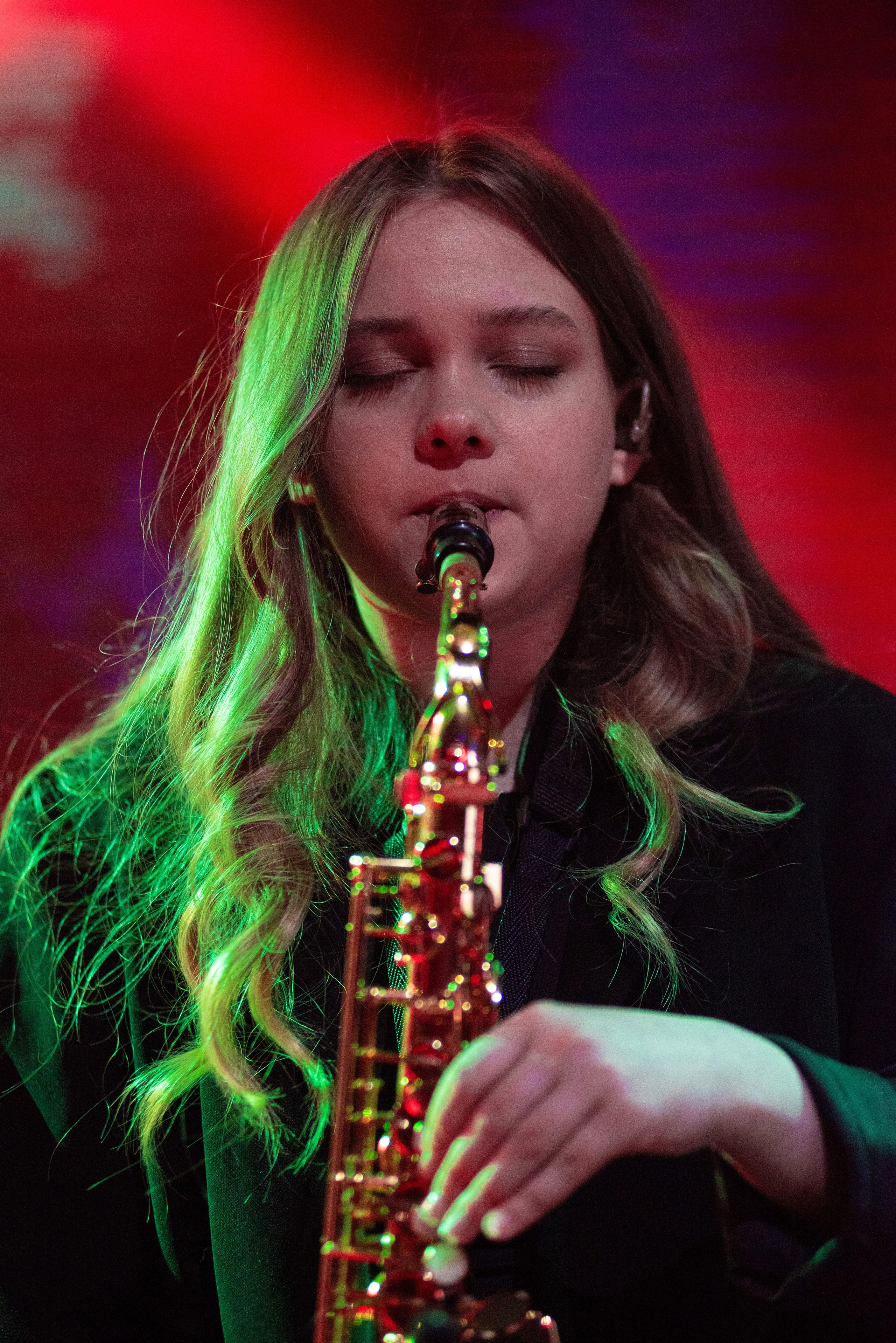 Саксофонистка группы «Лампабикт» крупным планом на фоне красно-зелёного концертного света
