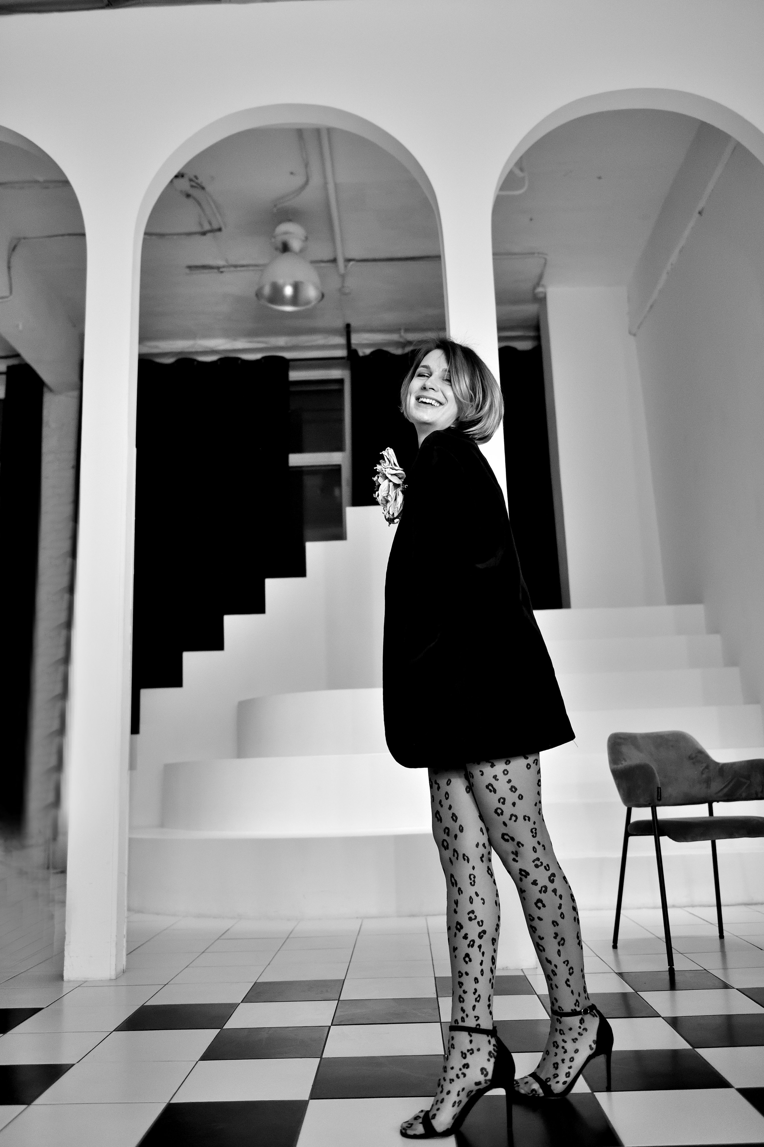 Девушка в пиджаке оверсайз и босоножках гуляет по полу в виде шахматной доски.