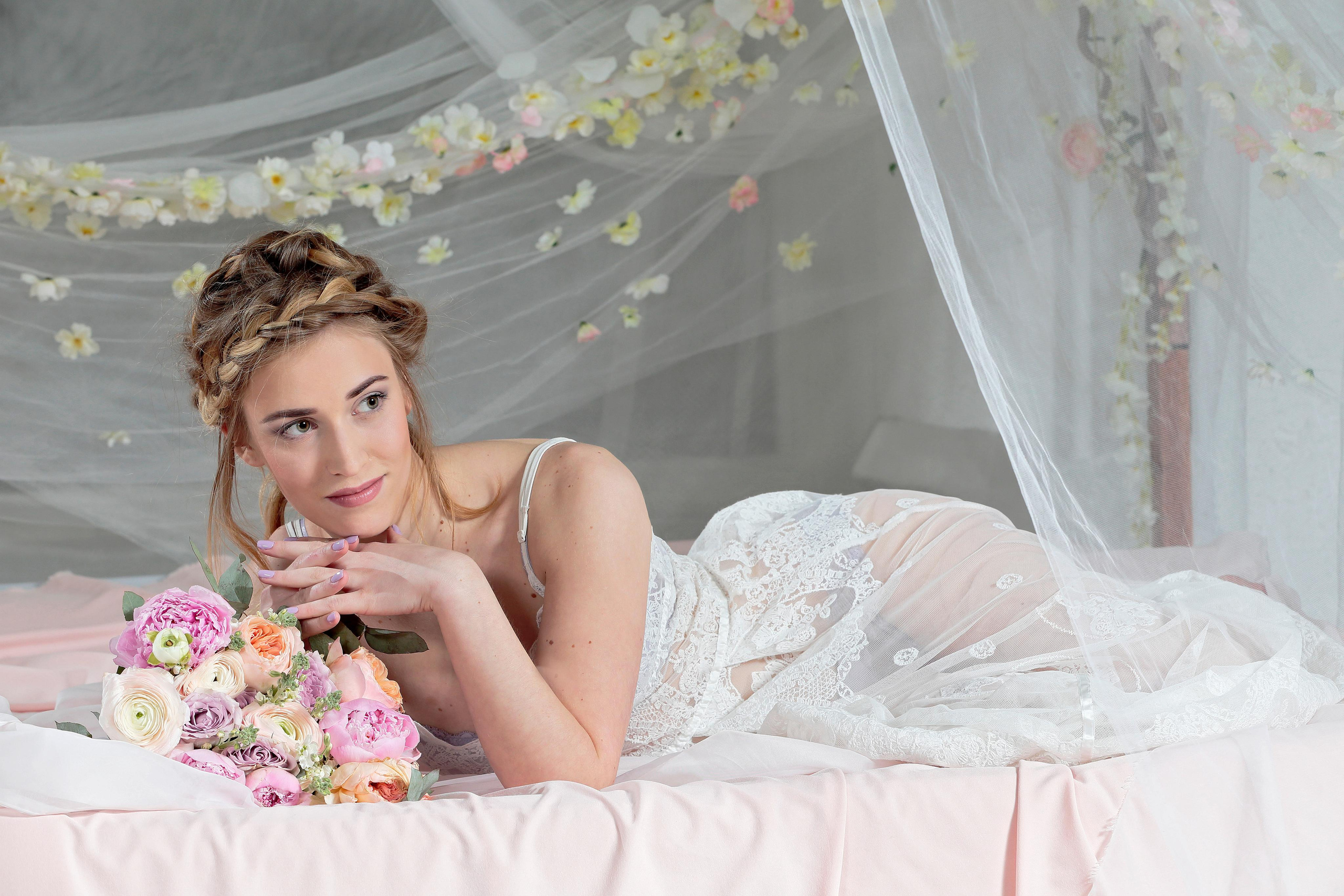 Девушка в прозрачной пижаме лежит на кровати с пологом.