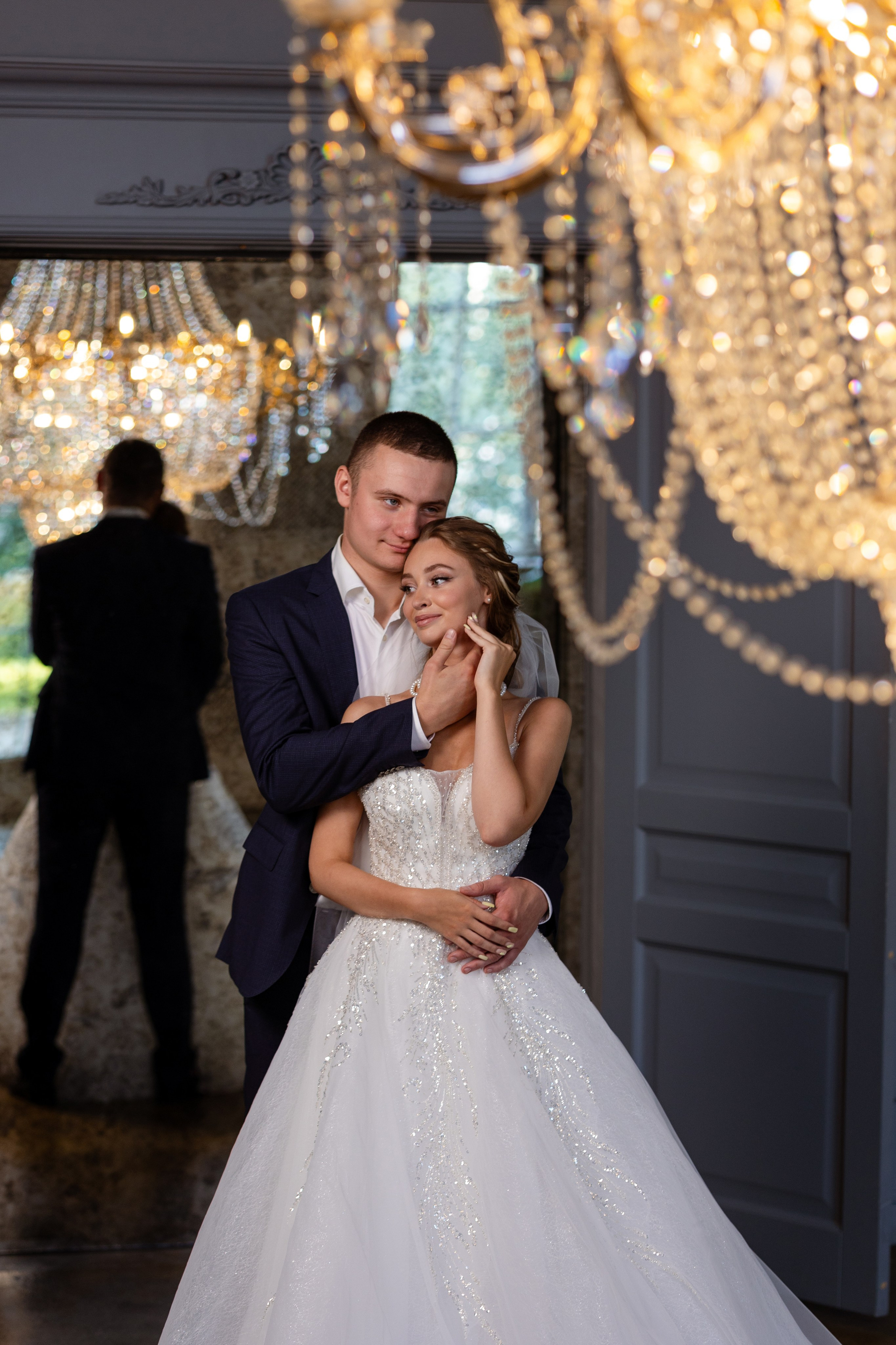 Молодые стоят в обнимку на фоне большого зеркала.