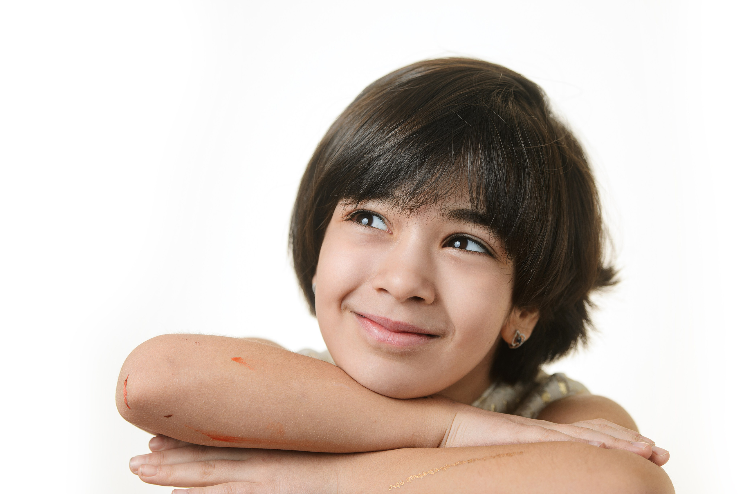 Портрет девочки с тёмными волосами: опирается на руки и улыбается на белом фоне.