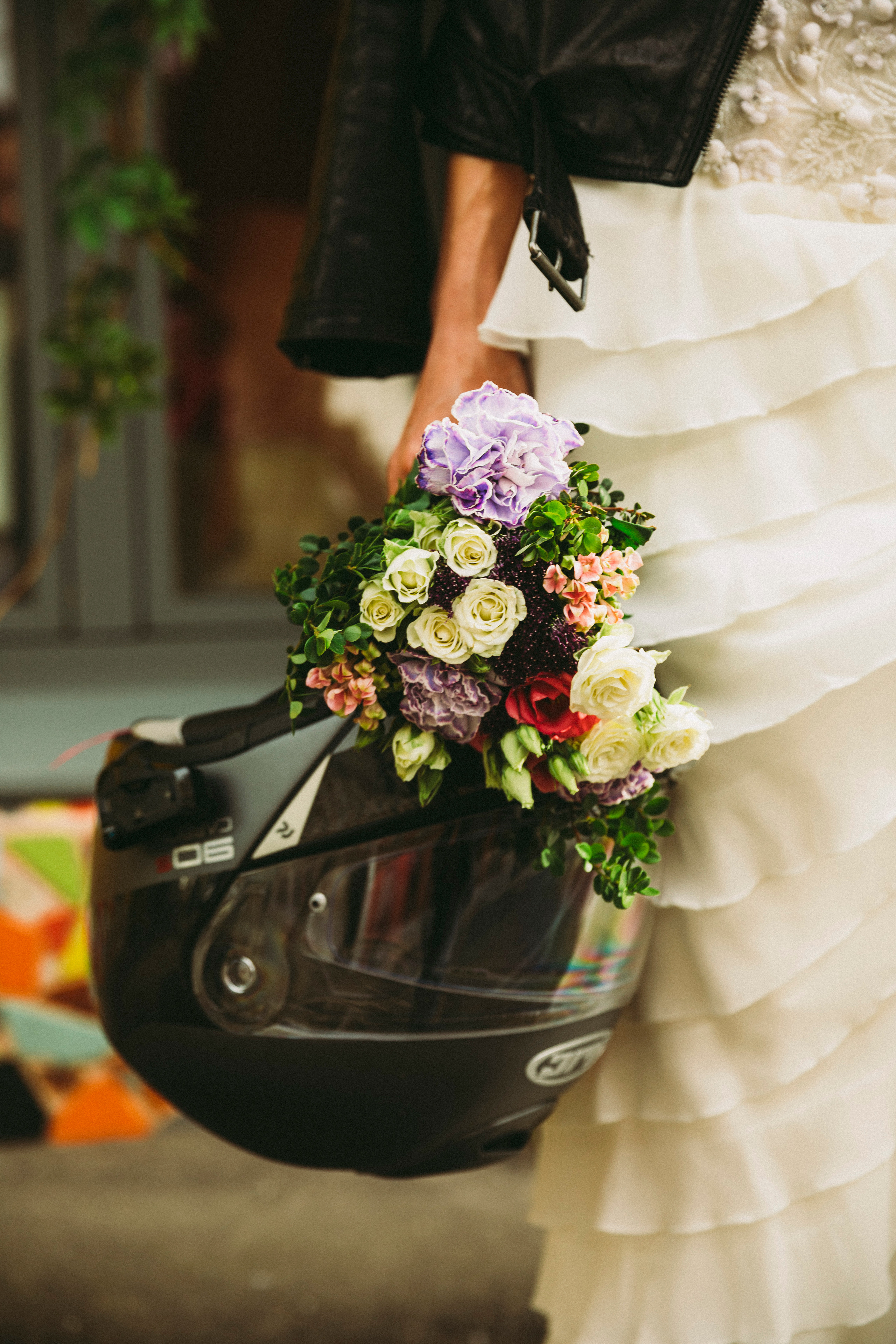 невеста держит в руках свадебный букет и шлем от мотоцикла