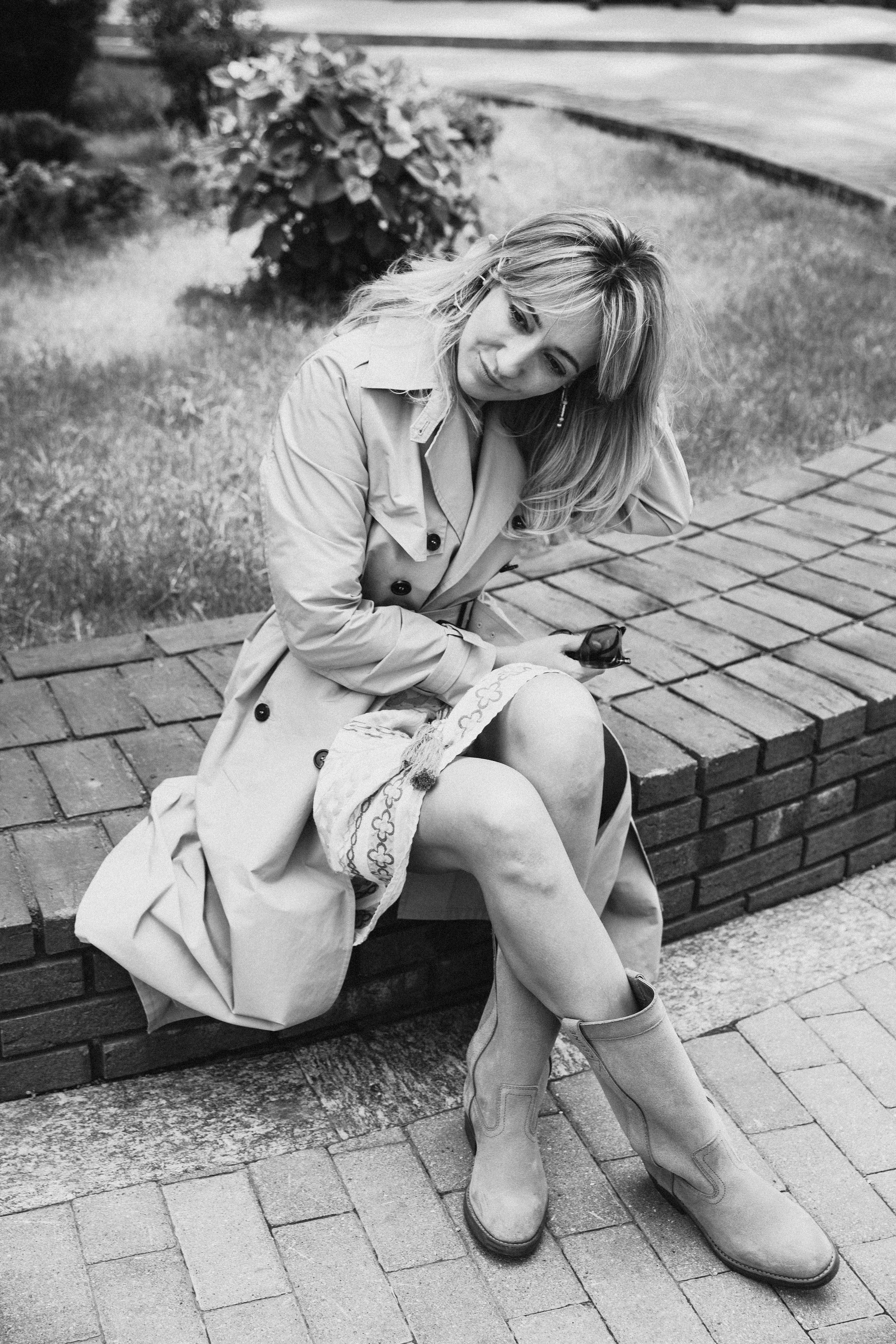 стильная девушка в платье и тренче  присела отдохнуть на лавочку