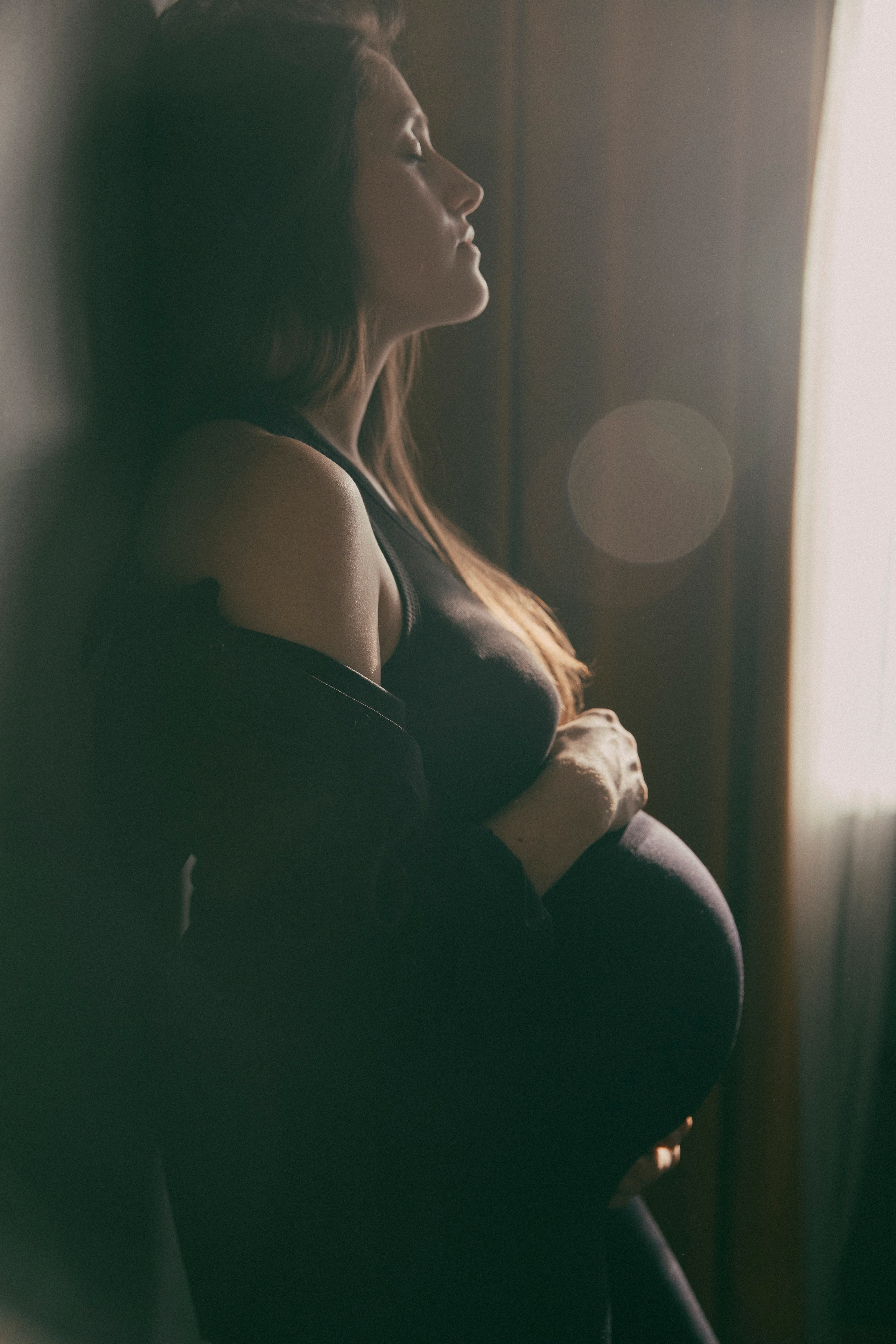 Красивая беременная девушка стоит около стены и смотрит в окно