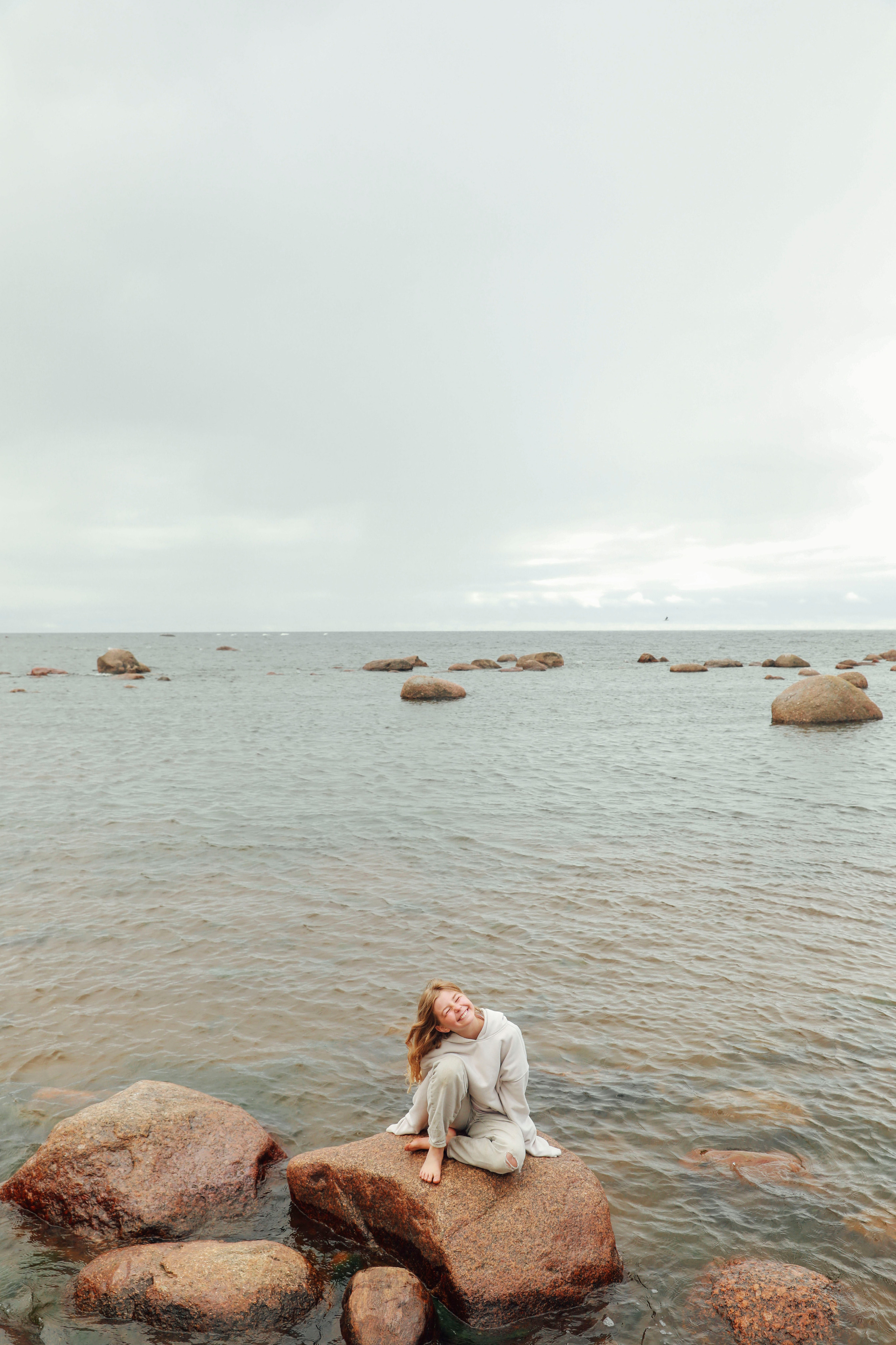 красивая девочка сидит на камне  в свитшоте и светлых штанах