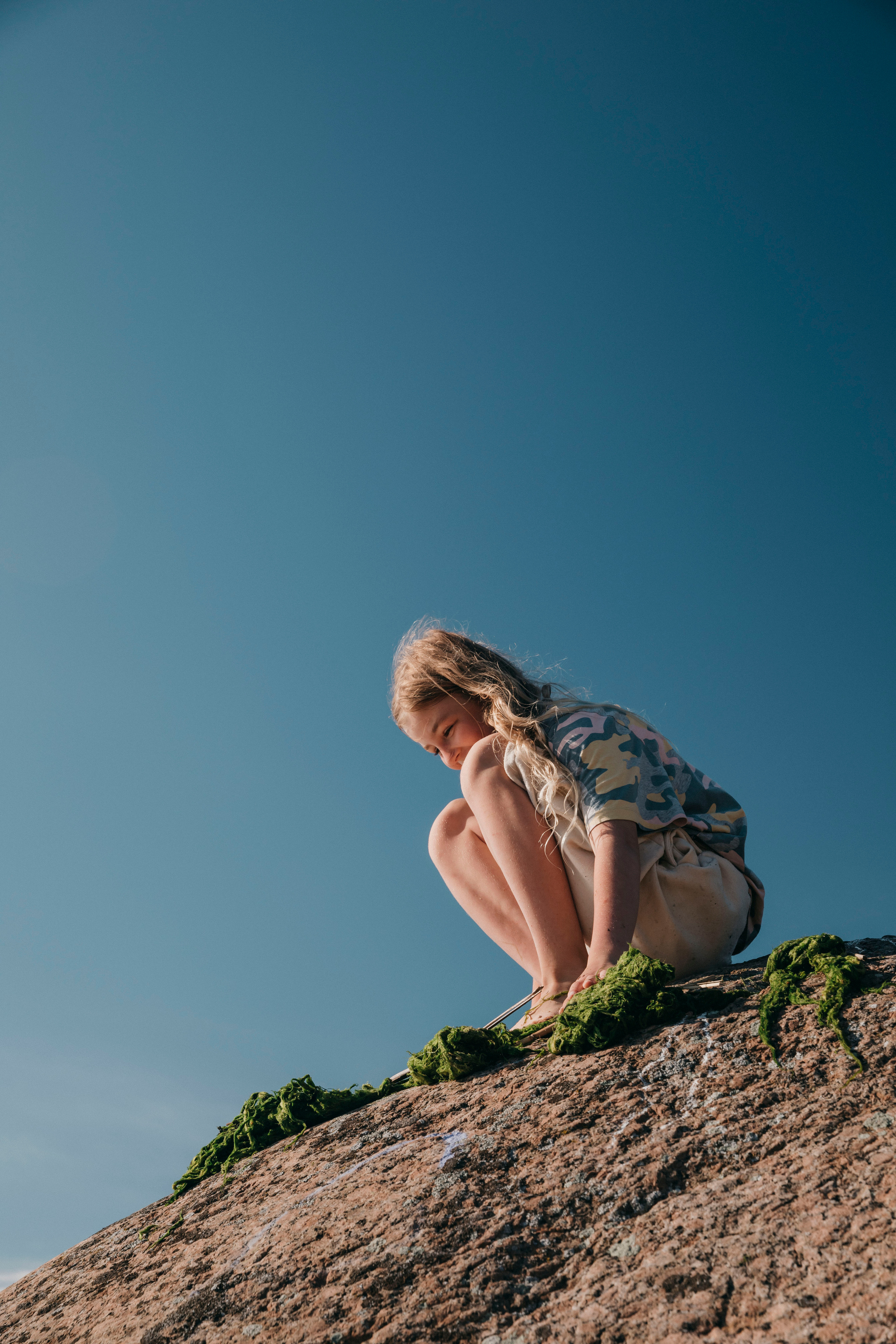 красивая меленькая девочка сидит на камне на берегу Финского залива