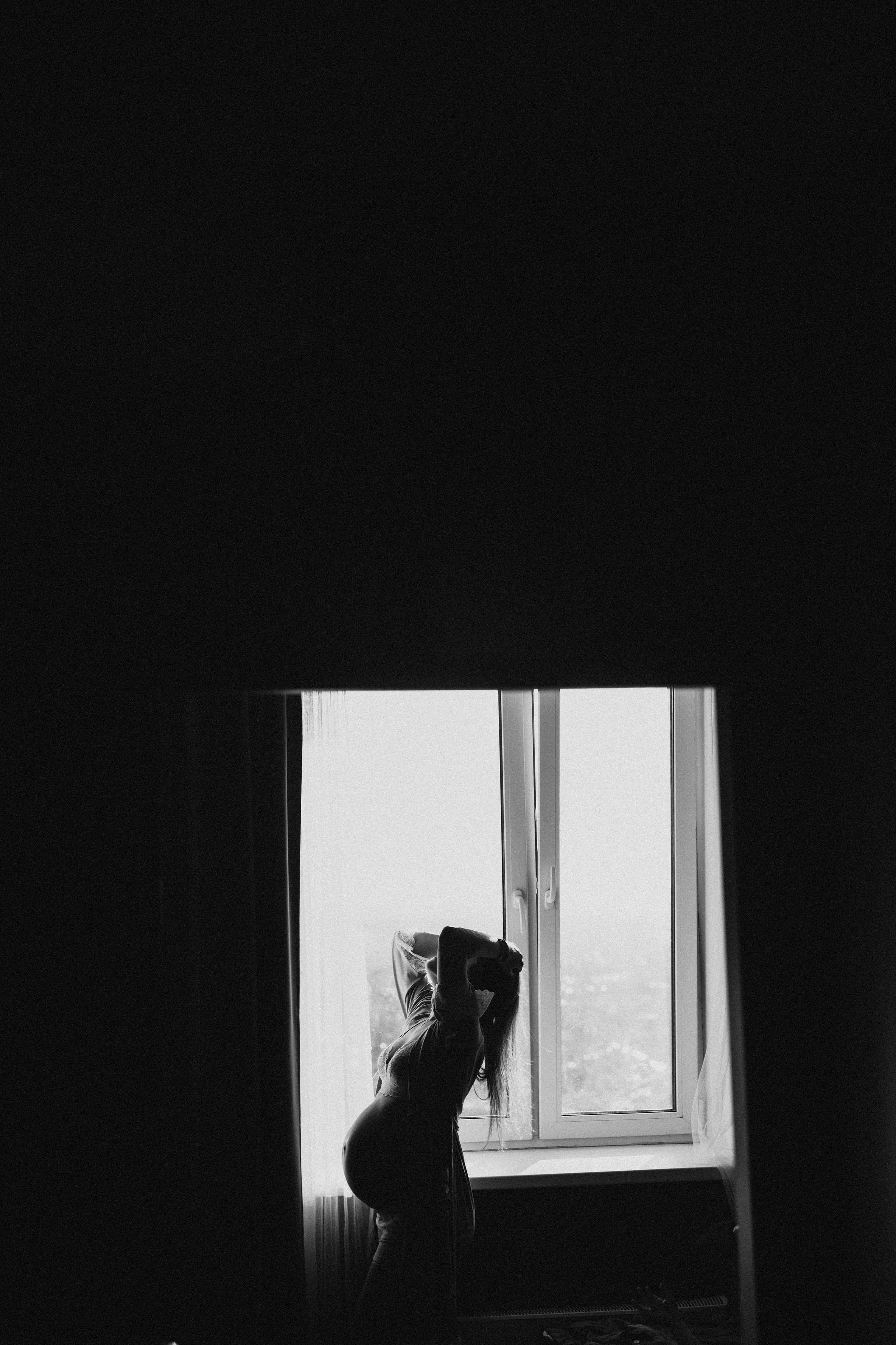 красивая беременная девушка стоит напротив окна у себя дома летом