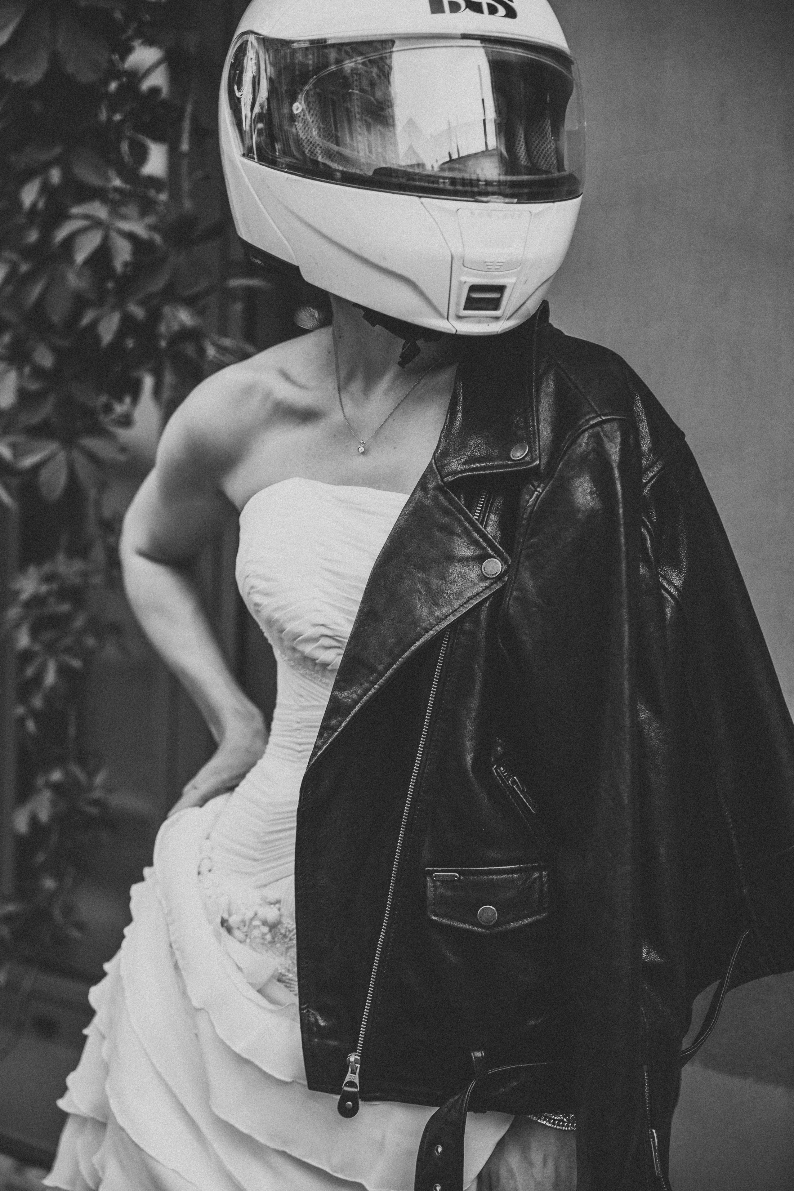 Невеста в красивом свадебном платье и кожанной куртке  и шлеме для мотоцикла стоит на улице Москвы летом вечером в теплую погоду и ждет своего жениха