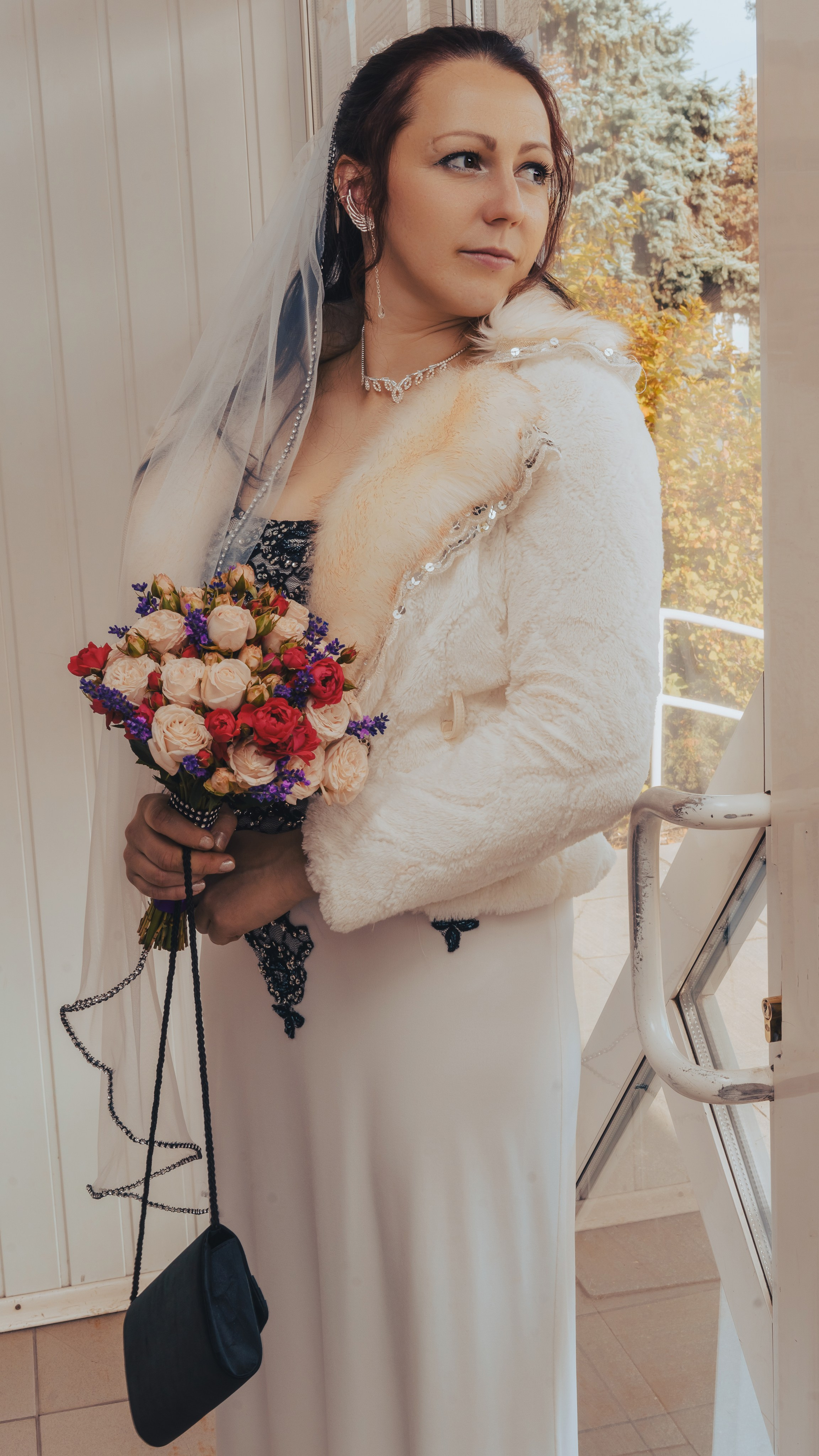 невеста с букетом цветов стоит у прозрачной двери