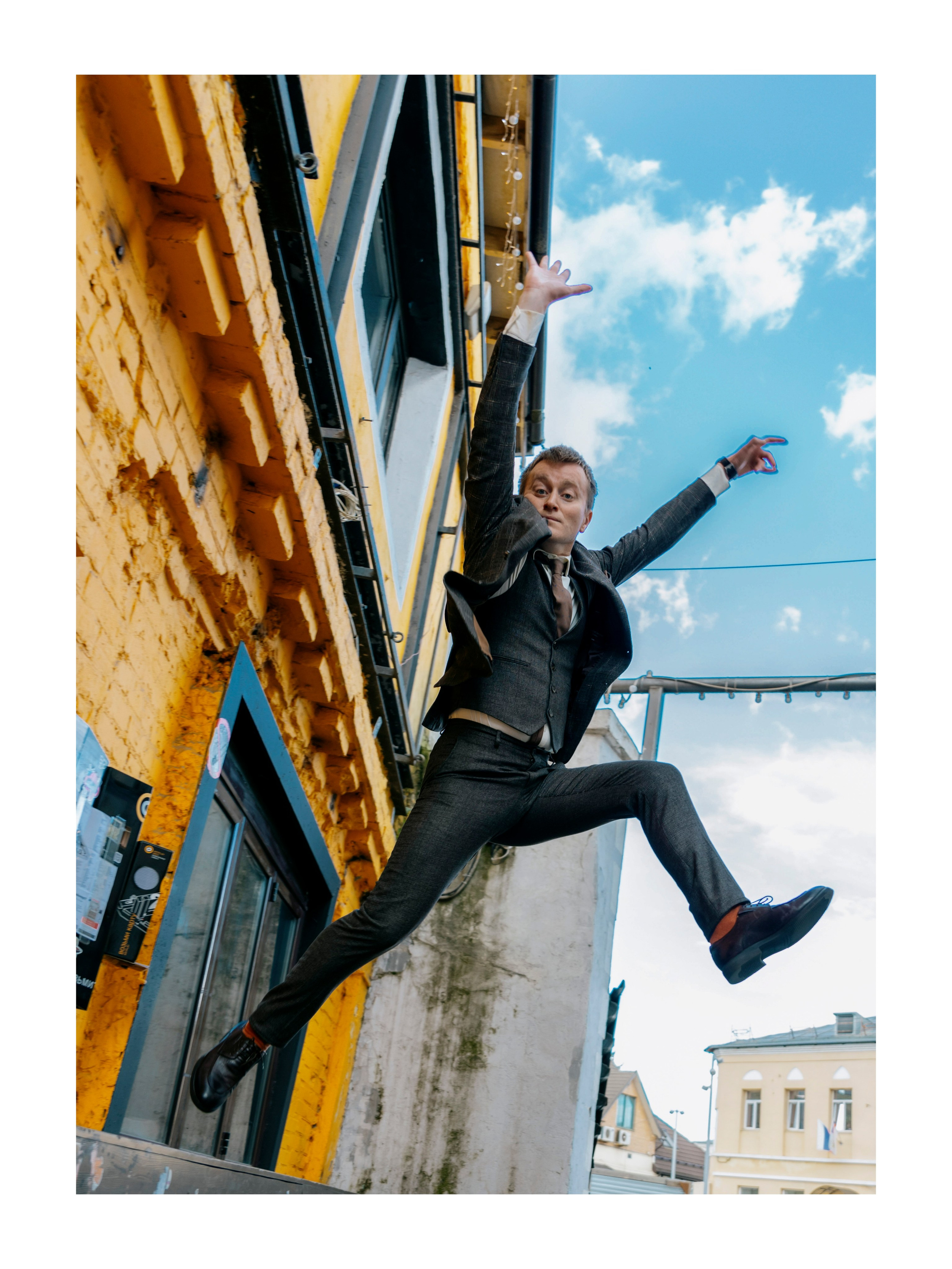 мужчина прыгает на фоне желтого здания и голубого неба, комический актер