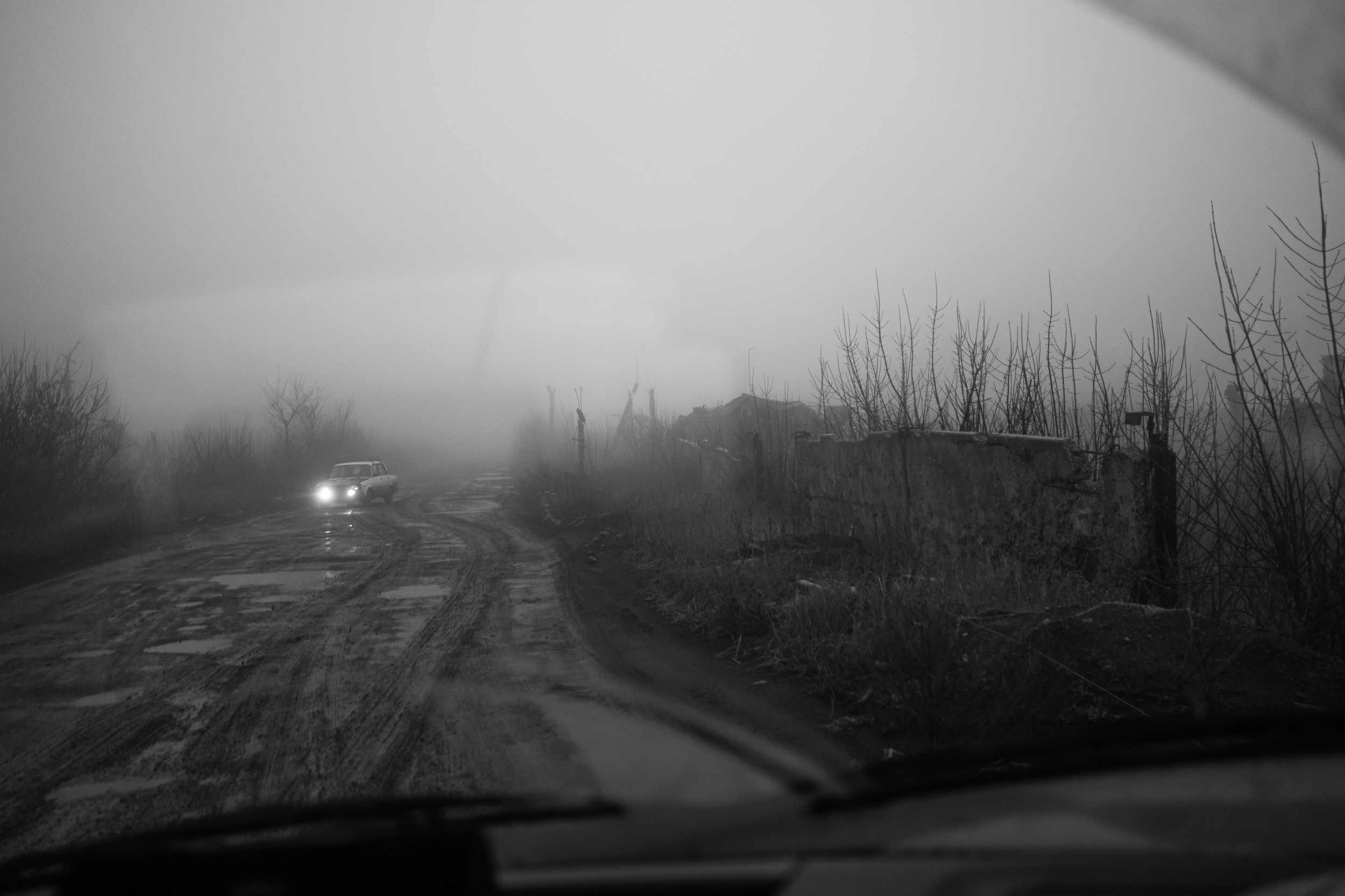 Осень 2025 года, ДНР. Первая поездка. Когда едешь по разбитой дороге, впервые заходишь в дом с дырой от ракеты, становится страшно и думаешь: какой кошмар. Но уже через месяц эти дома становятся знакомыми, а местные жители — близкими. И ты ловишь себя на мысли — так тоже нормально. Здесь тоже можно жить. Они живут там, где нет воды и света, но есть печки и кошки. Вместо стекол — затянутые пленкой окна. А еще — постоянная опасность, обстрелы и желание жить дальше. Несмотря ни на что, люди продолжают готовить борщ и  выращивают цветы. И ты тоже постепенно привыкаешь.То, что с первого взгляда — кошмар, через месяц становится бытом. Война никуда не делась. Она стала фоном. Но остались люди. И они продолжают жить.                                                                                                                                      1. Встречная. Я ехала туда. Кто-то ехал оттуда. Мы разминулись в тумане.