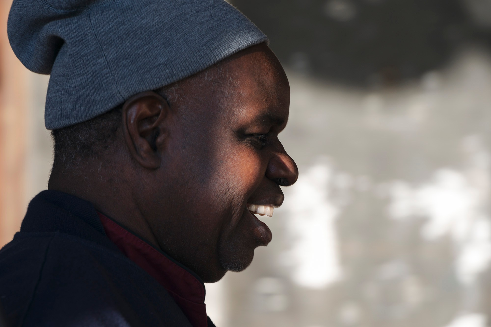 Портрет темнокожего человека в профиль в мягком боковом свете, улыбающегося и погружённого в тёплое настроение.