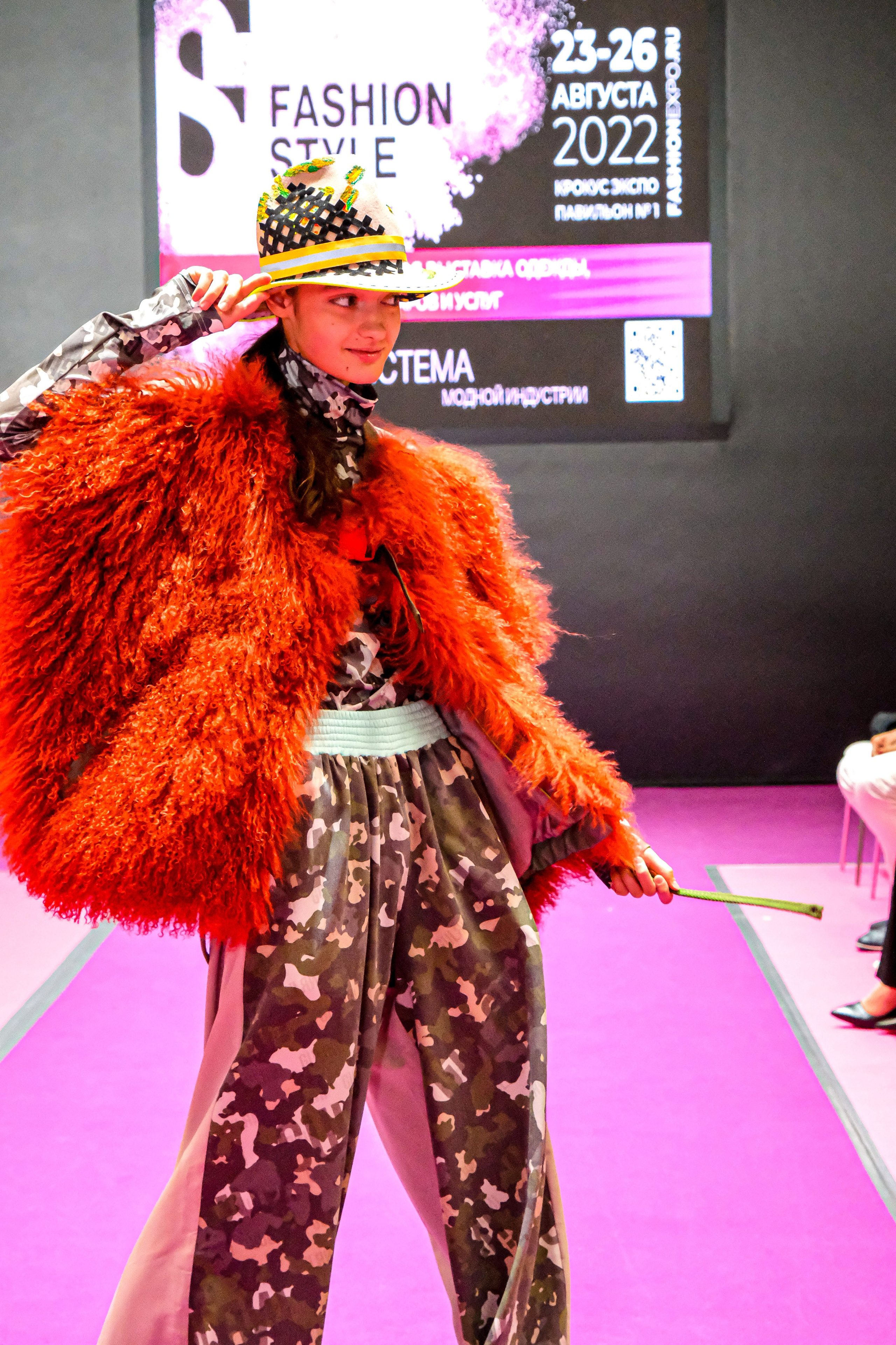  "Модели в ярких нарядах проходят по подиуму во время показа мод, освещенные яркими софитами и окруженные восторженными зрителями."