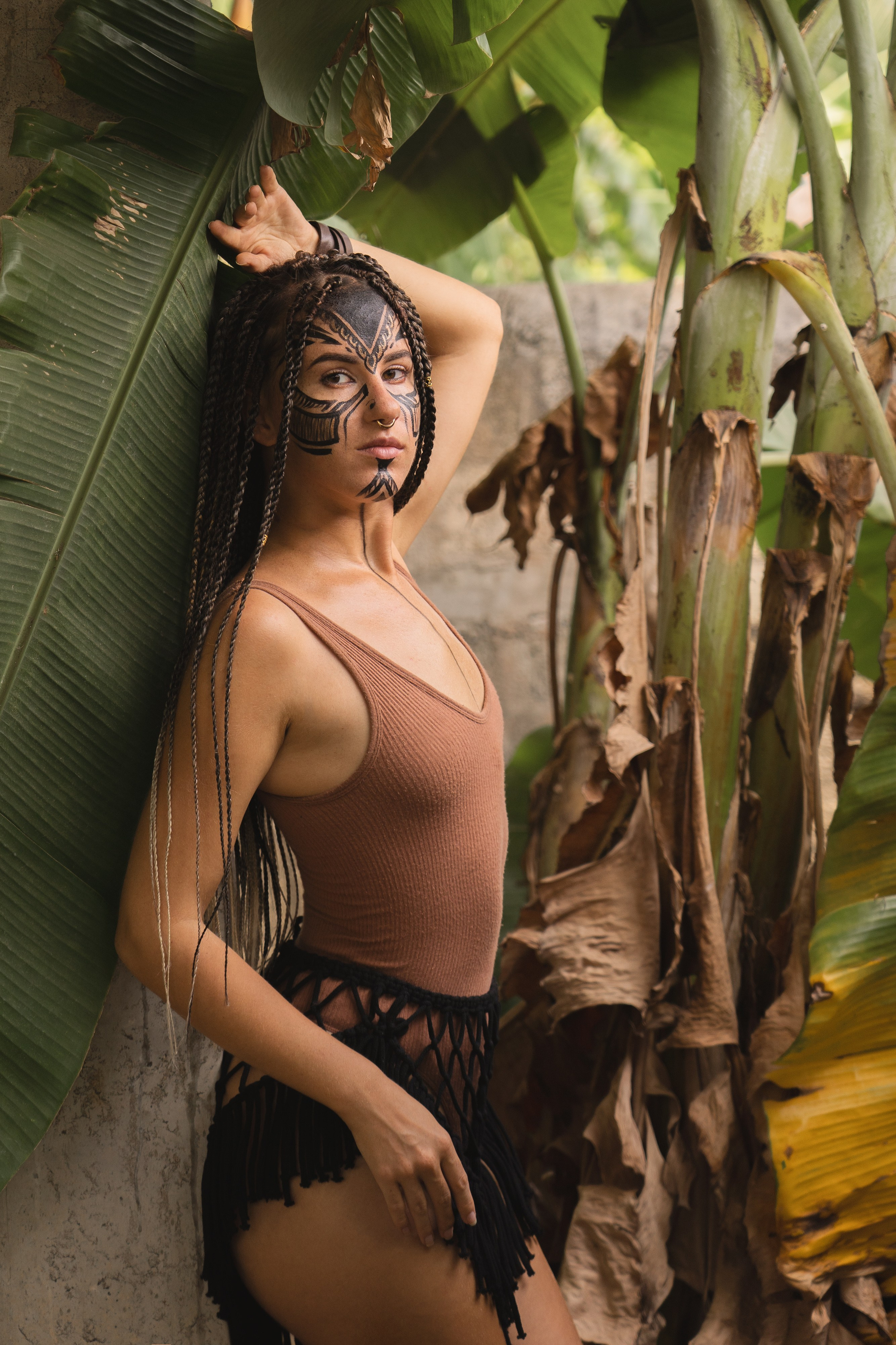 a girl with braids and face paint surrounded by greenery and tropical flora