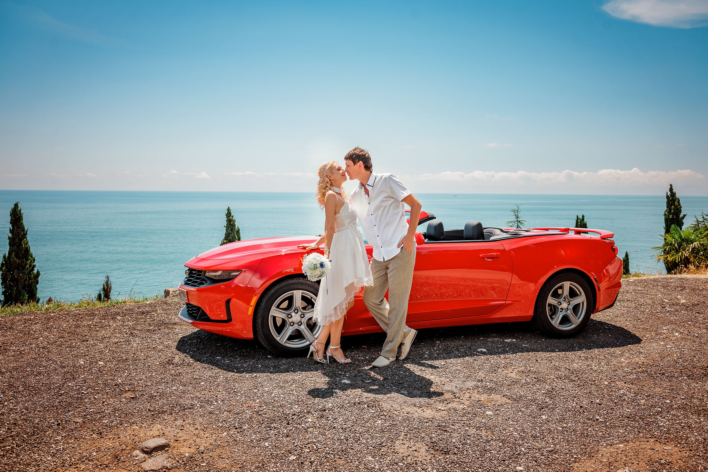Красный кабриолет и пара на фоне лазурного берега.