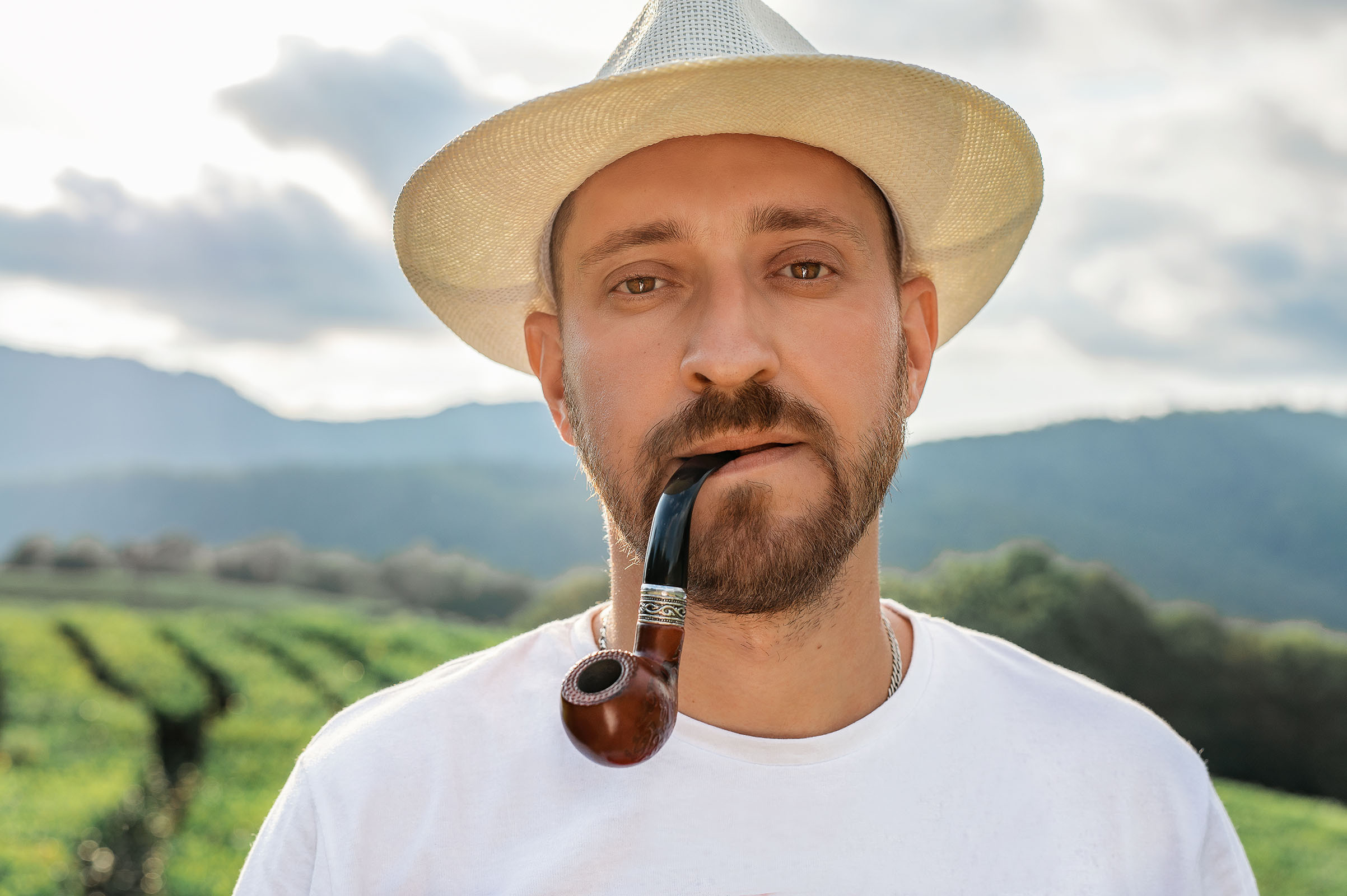 Мужчина с трубкой в шляпе на фоне чайных плантаций.