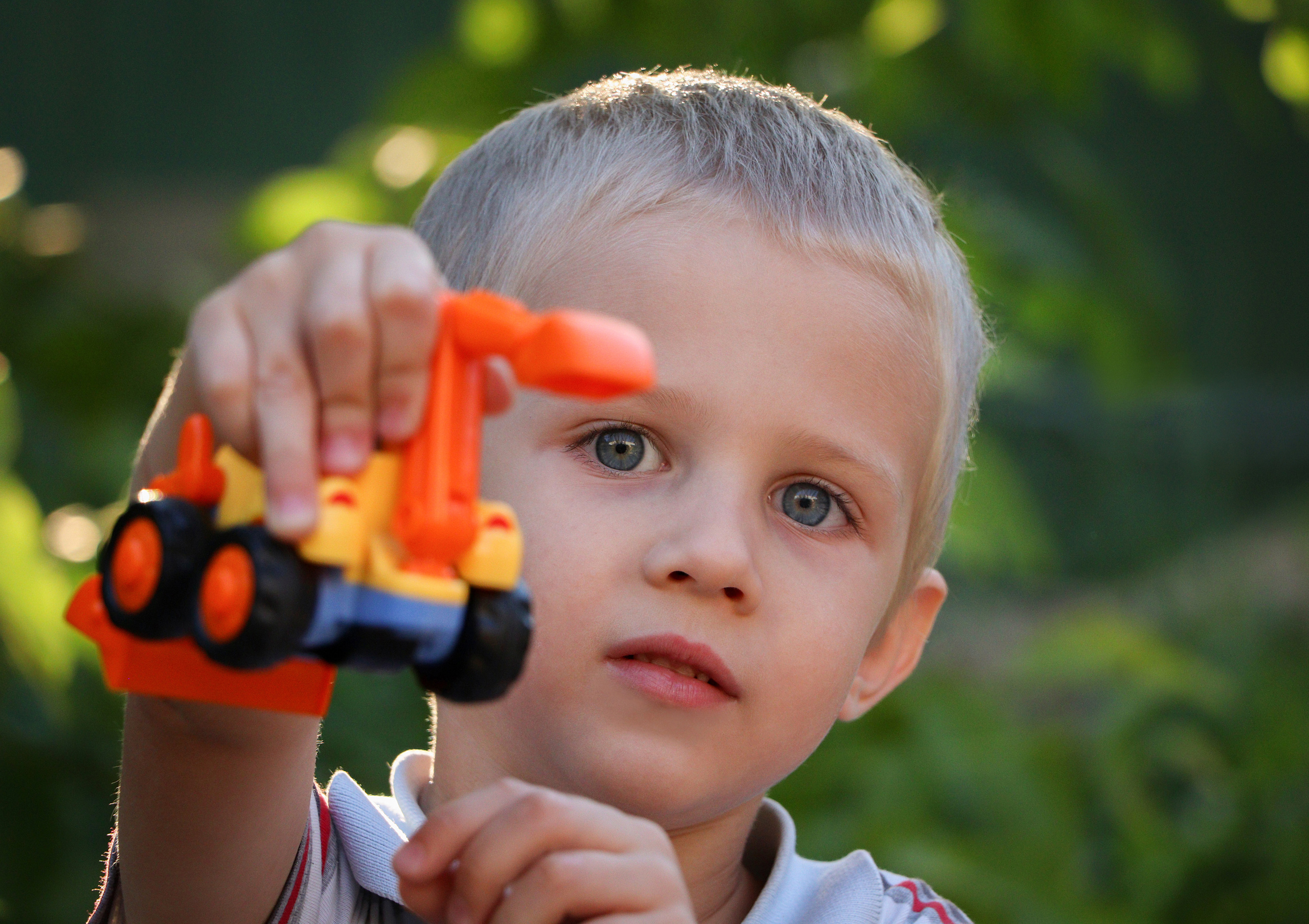 детский портрет на фоне зелени, в руках у ребенка игрушка