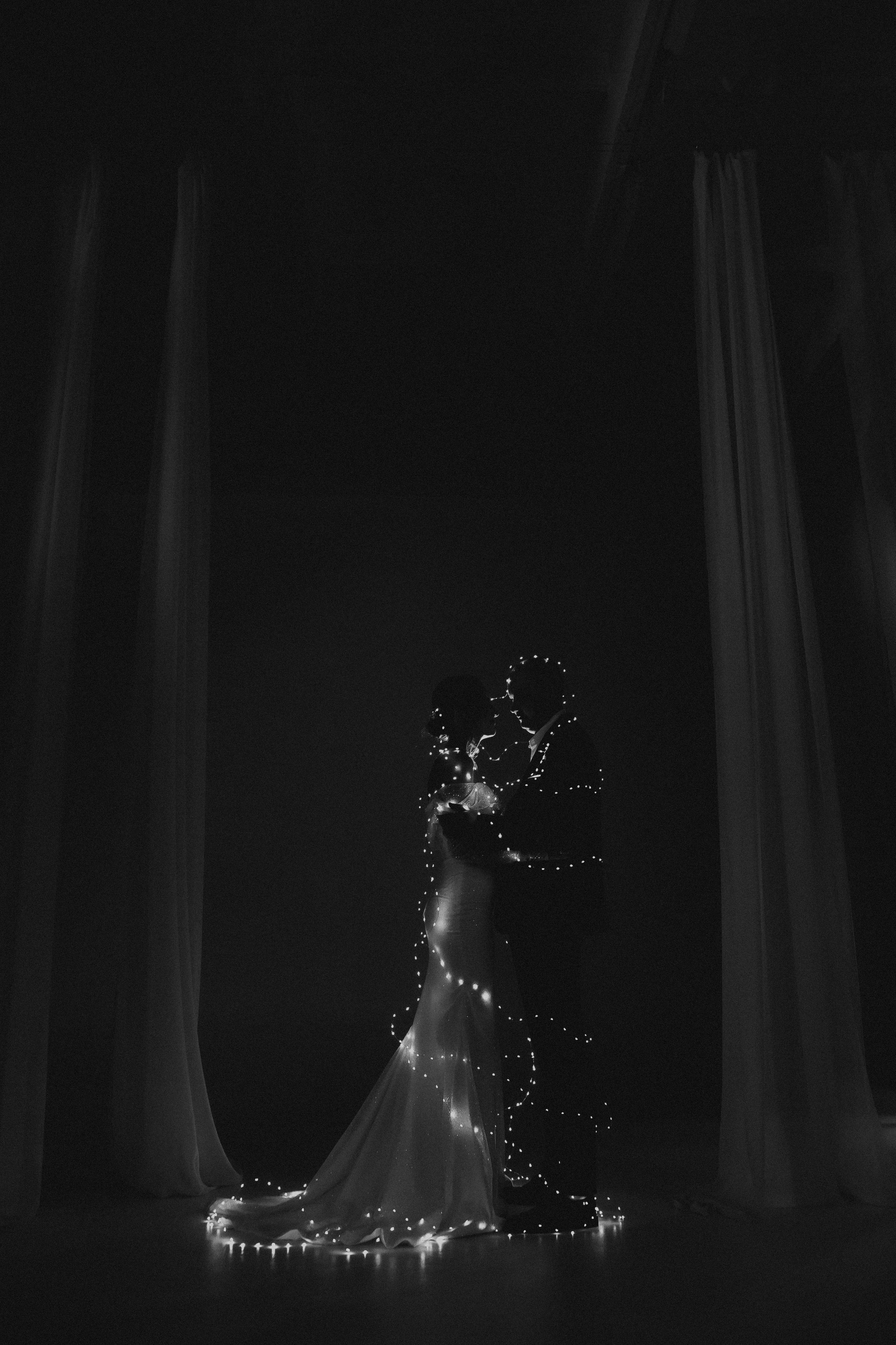 Черно-белая фотография молодожены обнимаются в полный рост обмотаны гирляндой