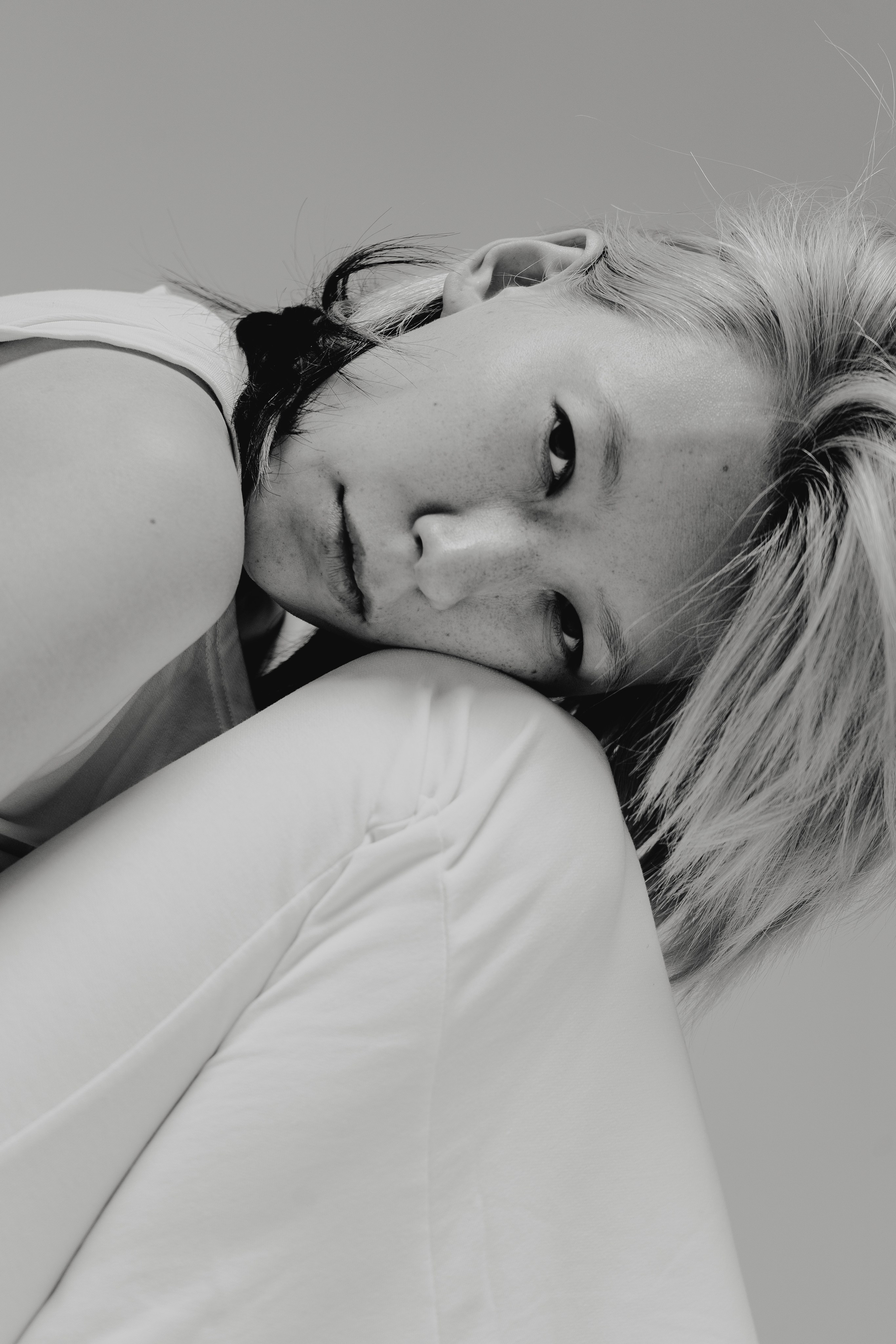 Девушка положила голову на колено и смотрит в объектив