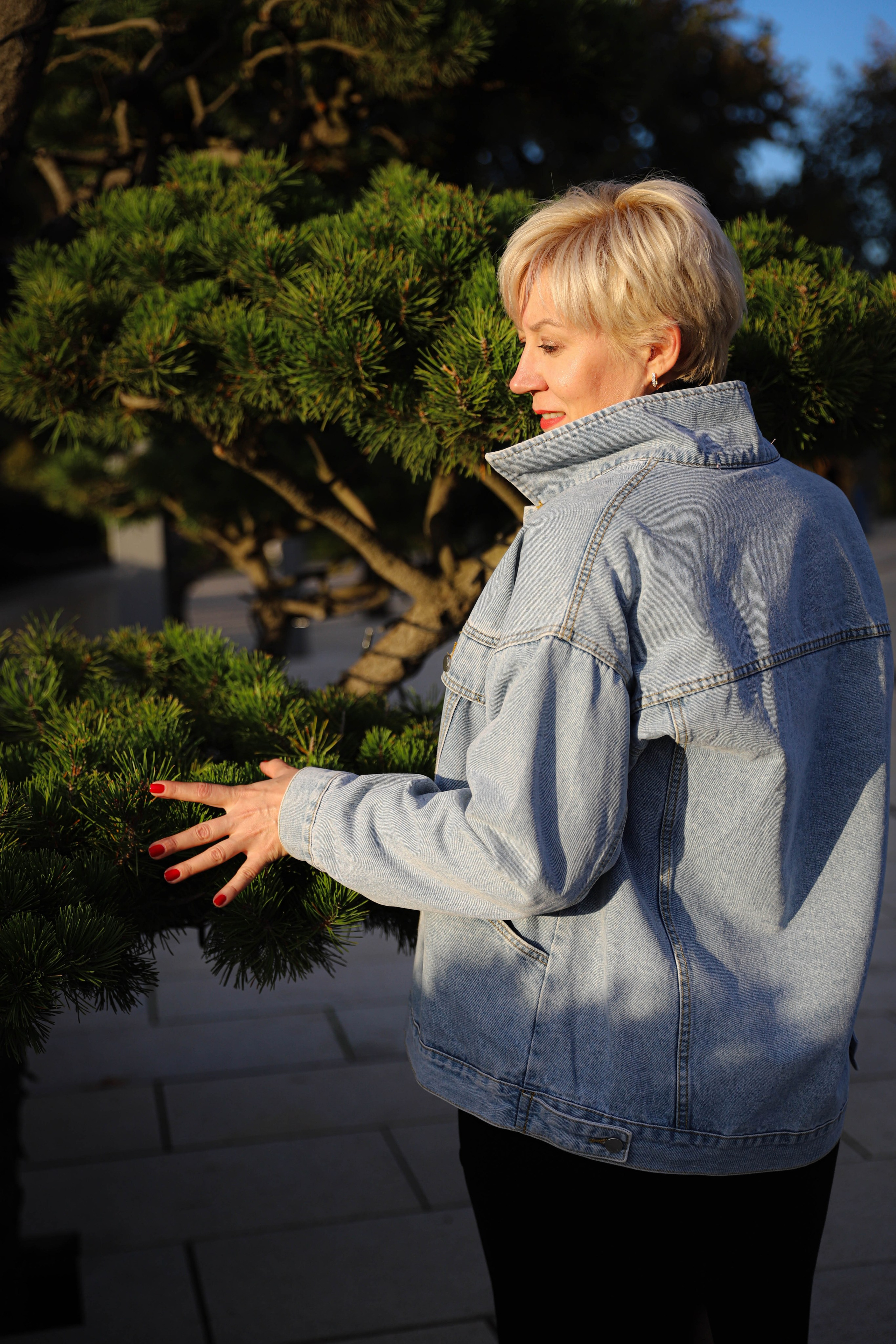 Фотосессия в парке: девушка в джинсовой куртке обнимает дерево, восхищаясь красотой осени.